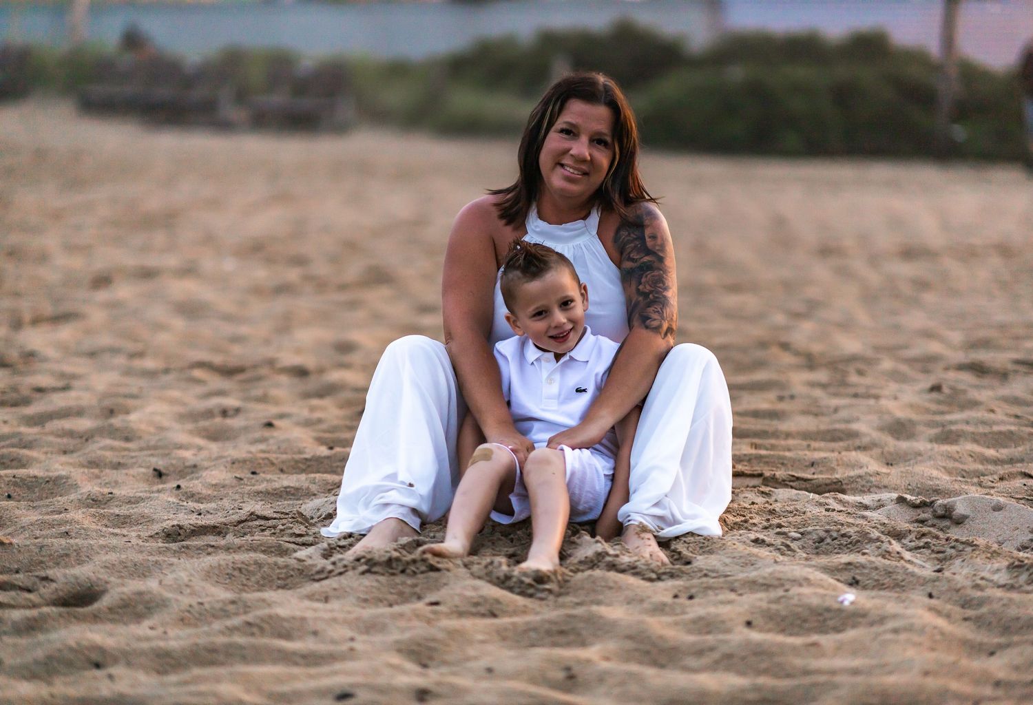 A parent and child share a tender moment sitting together on a sandy beach.