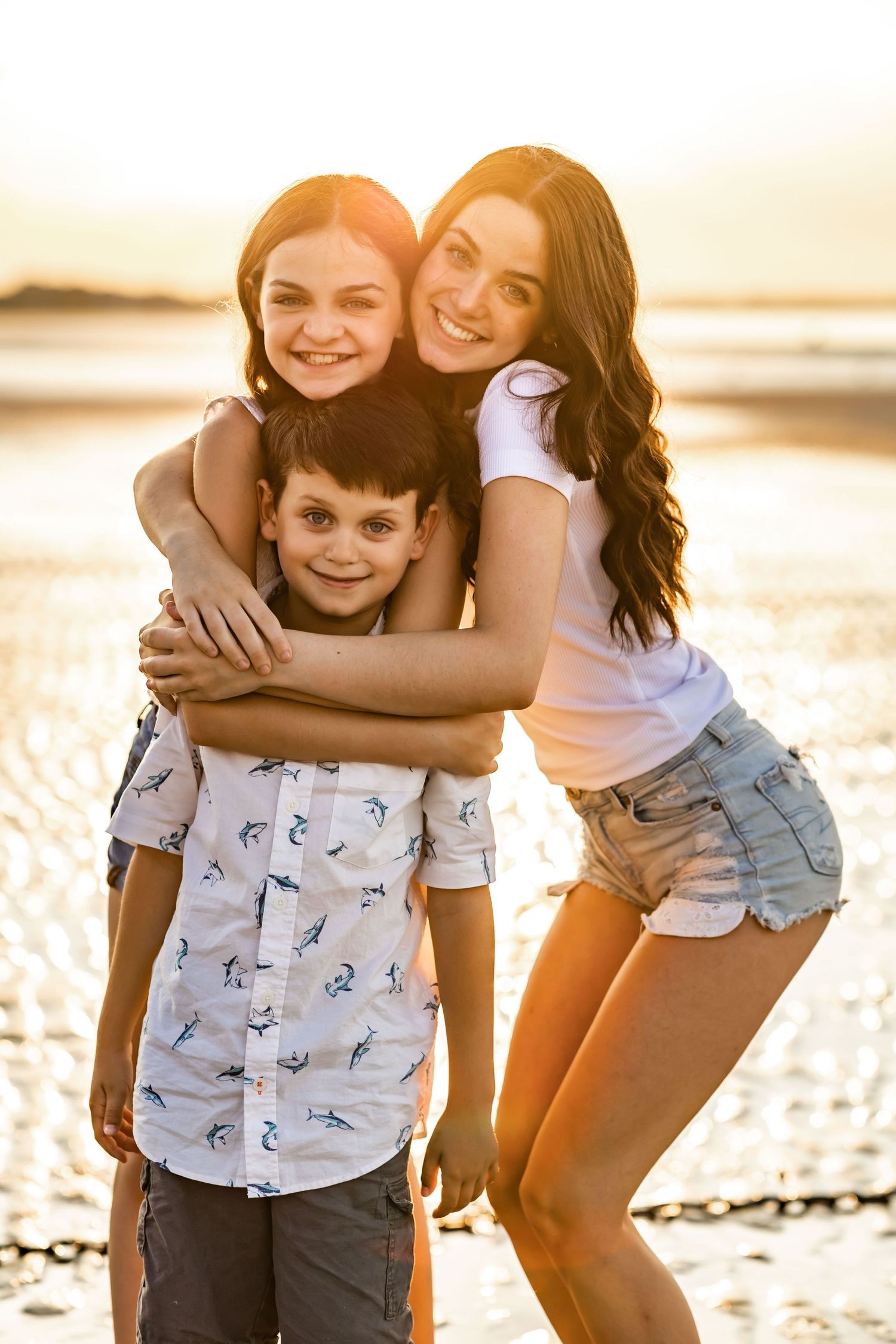 Family embracing on beach during golden hour sunset.