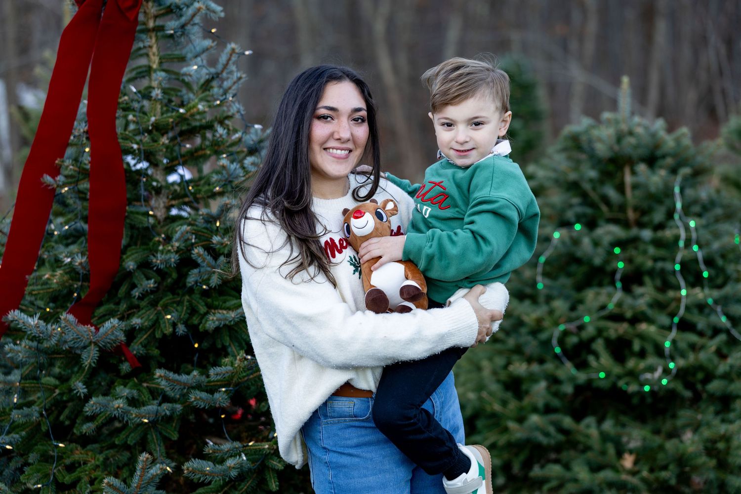 Holiday family portraits taken in front of evergreen trees with festive decorations.