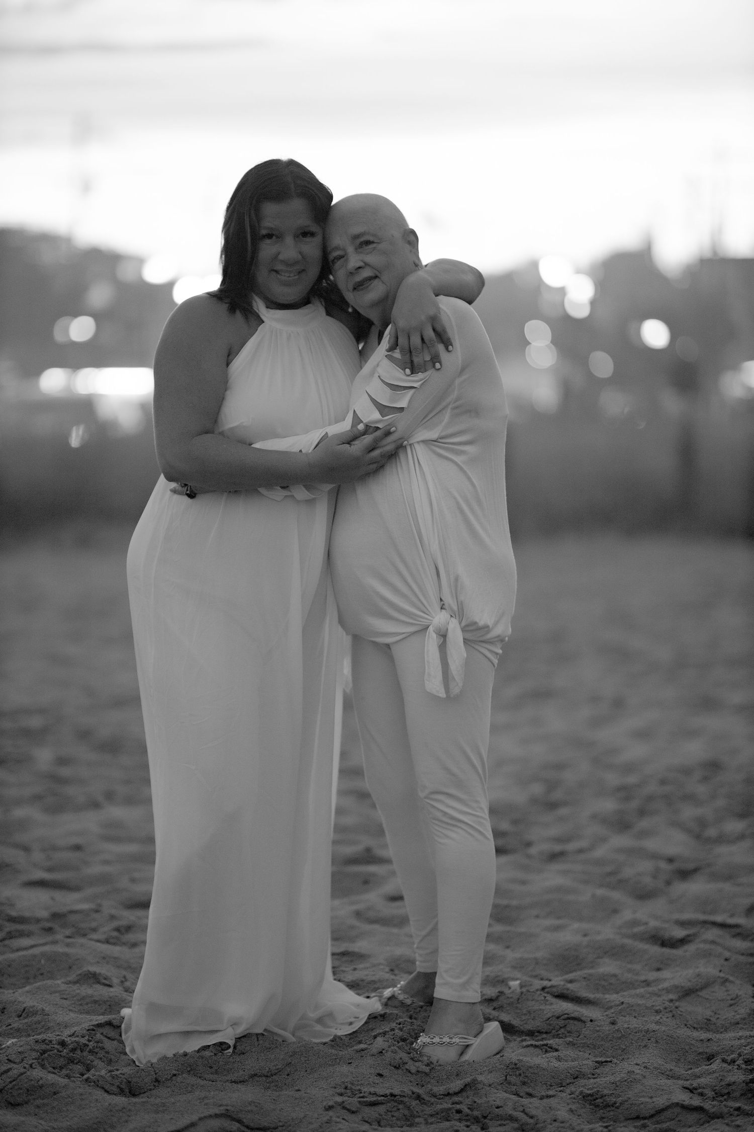 Couple in white outfits embracing on beach at dusk.