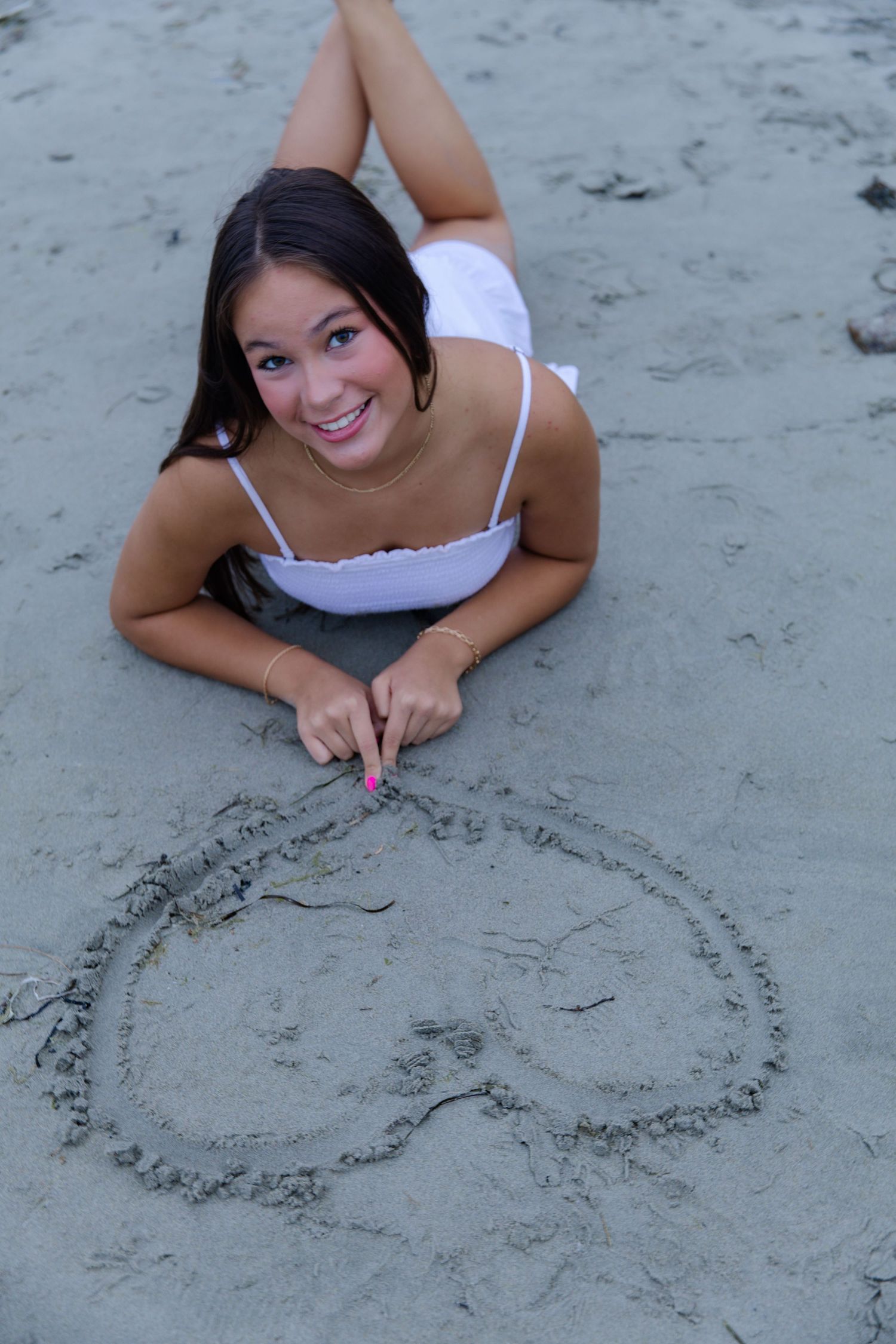 Person lying on beach sand drawing a heart shape.