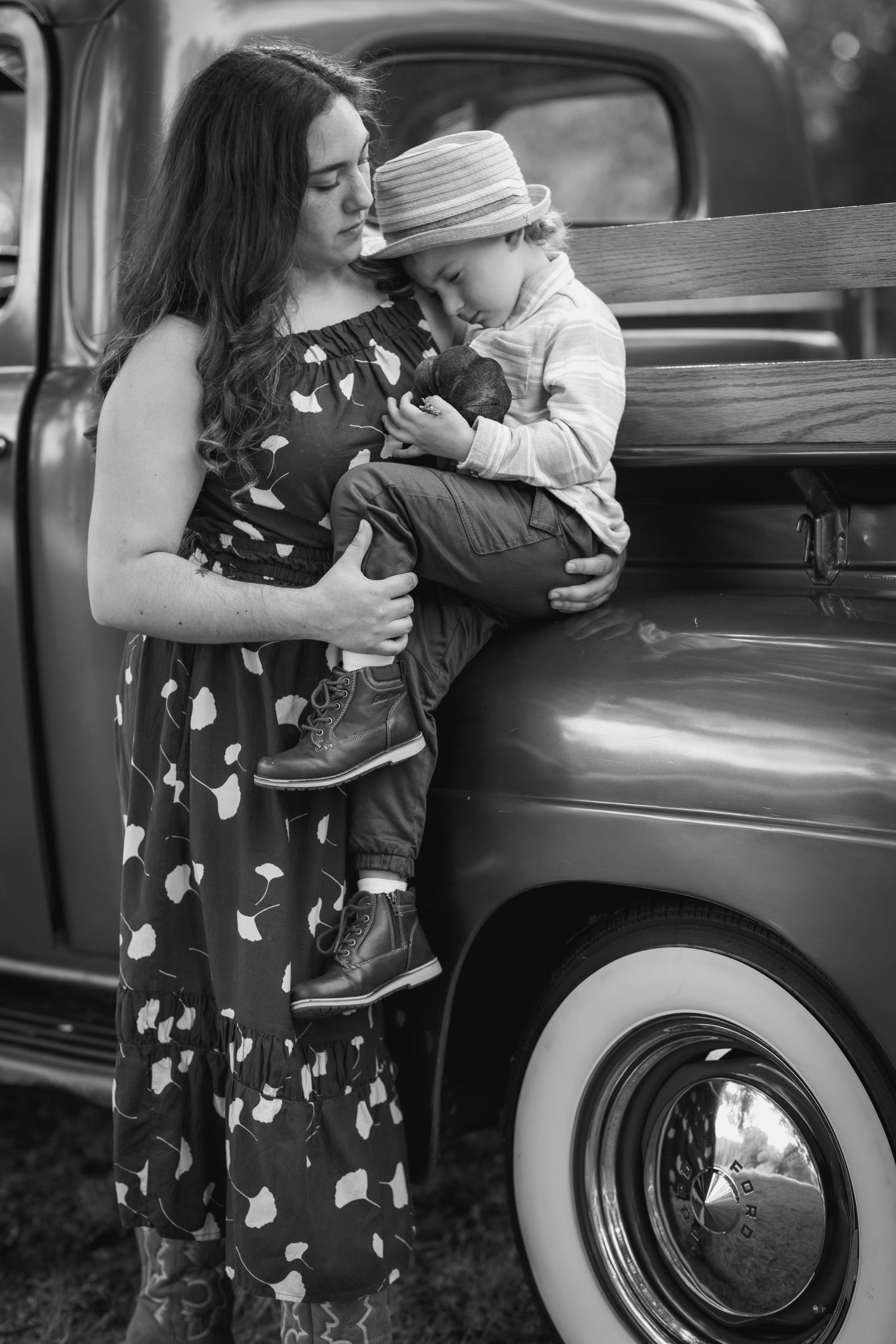 Woman in floral dress standing beside vintage car during outdoor photo session.