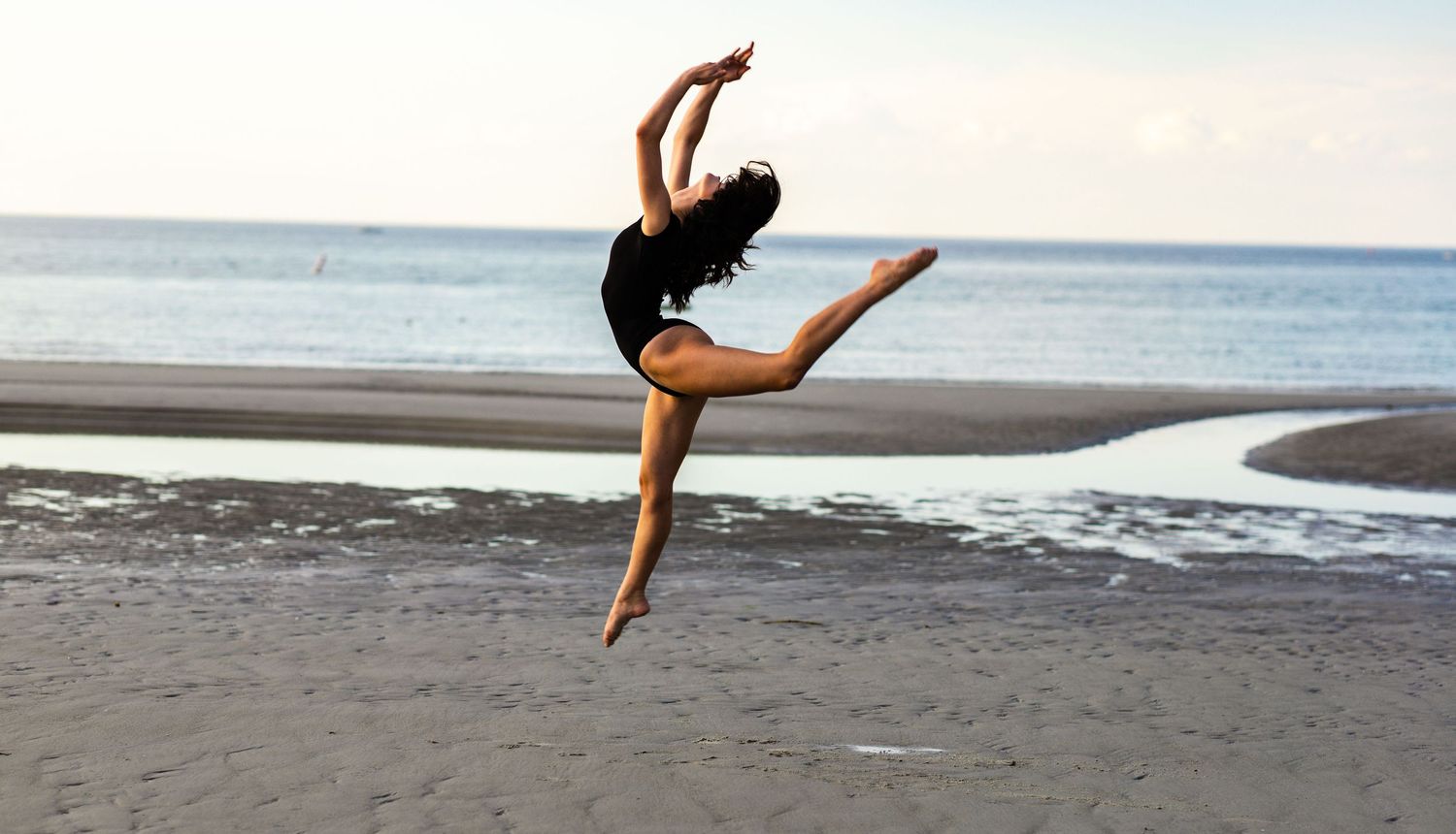 Dancers leaping and posing on a beach boardwalk at sunset.
