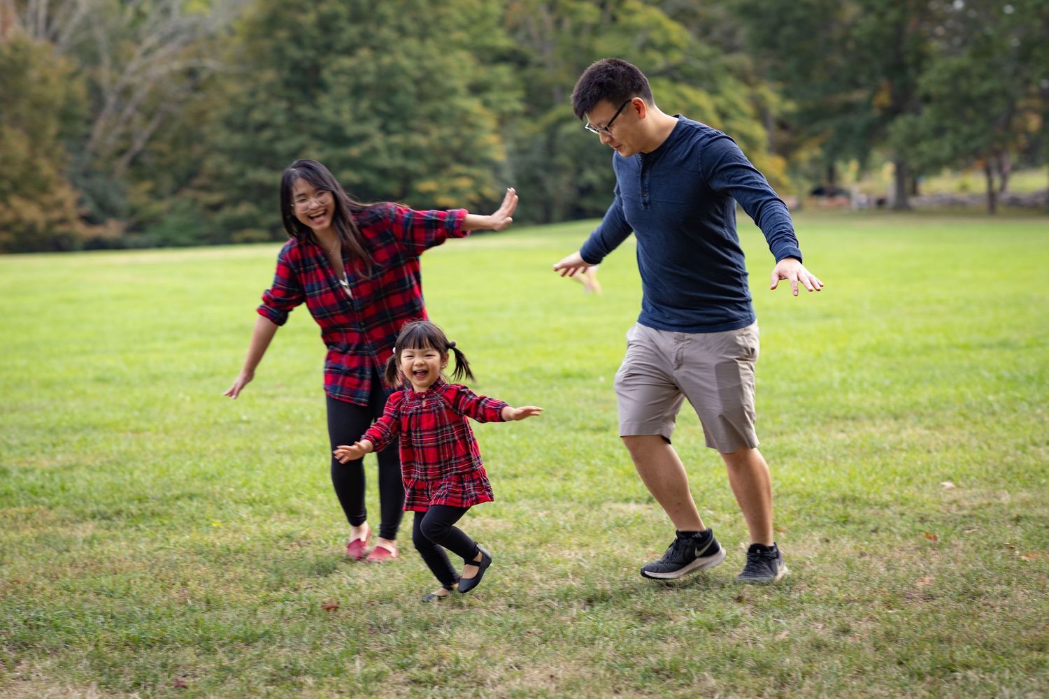 Family playing and running together on grassy field during autumn day.
