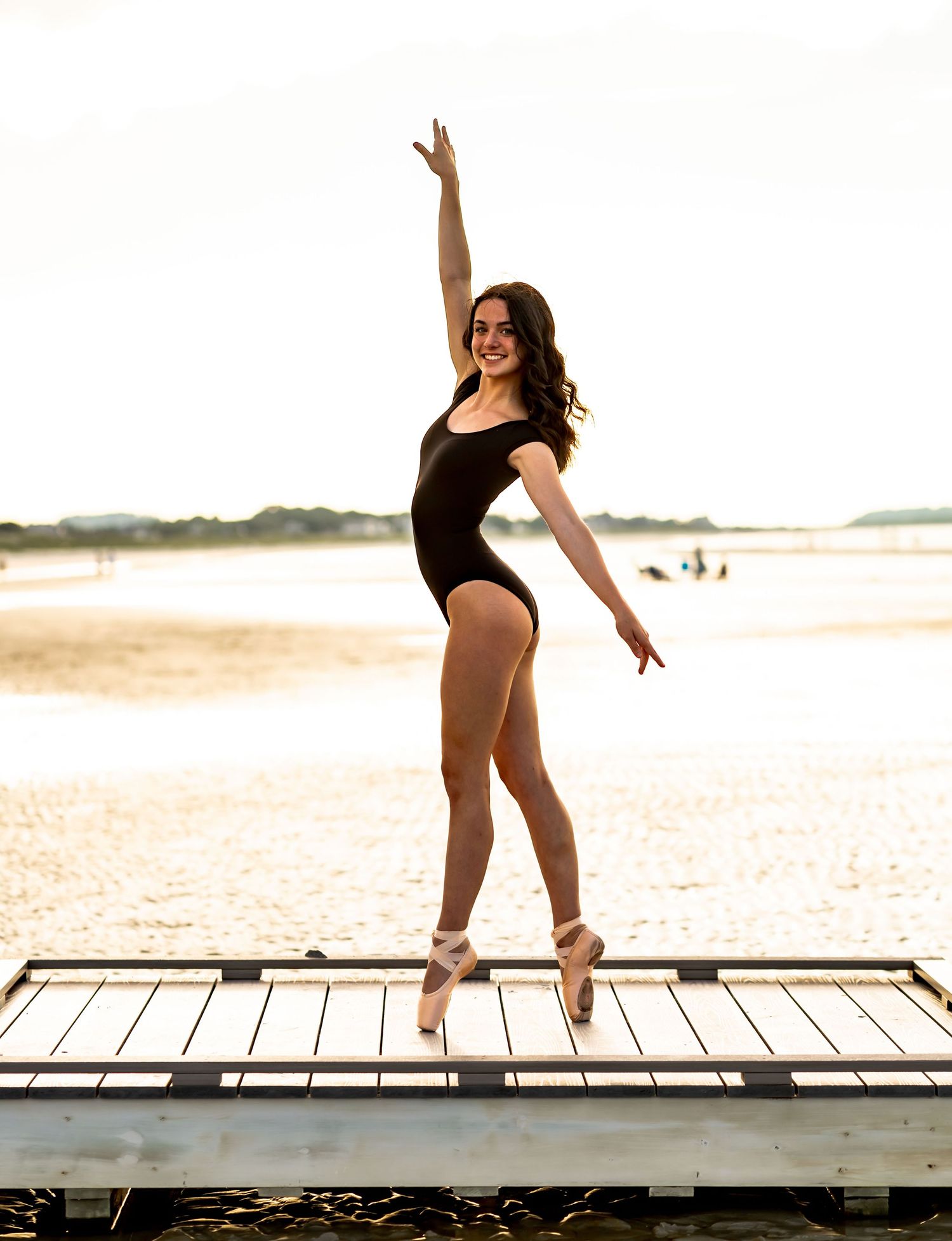Dancers performing graceful poses on a wooden boardwalk by the ocean.