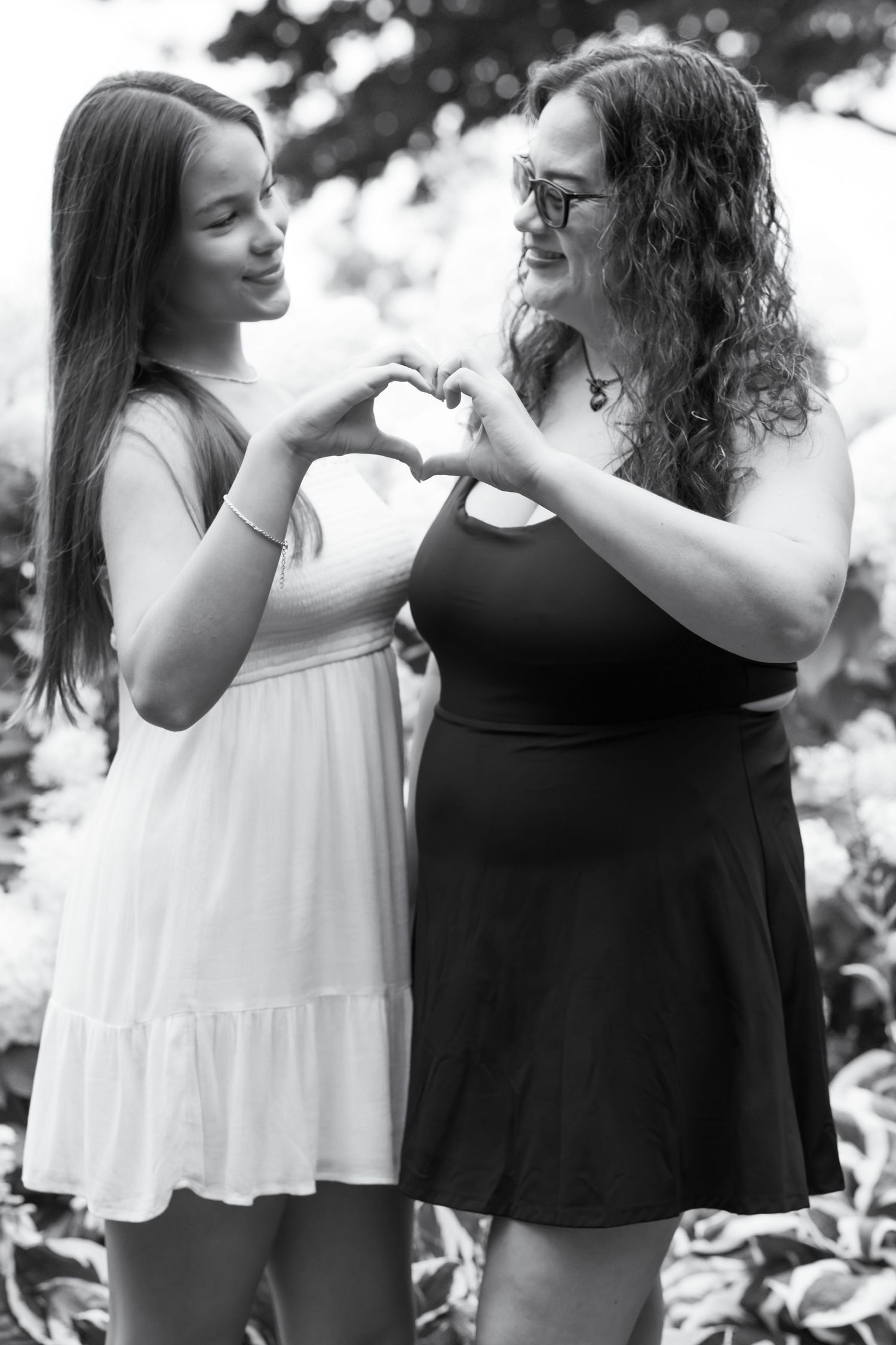 Two friends in summer dresses making heart shape with hands outdoors.
