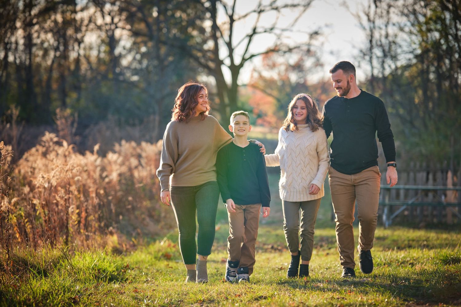 Family of four walking together outdoors in autumn park, smiling and enjoying nature on a sunny day.