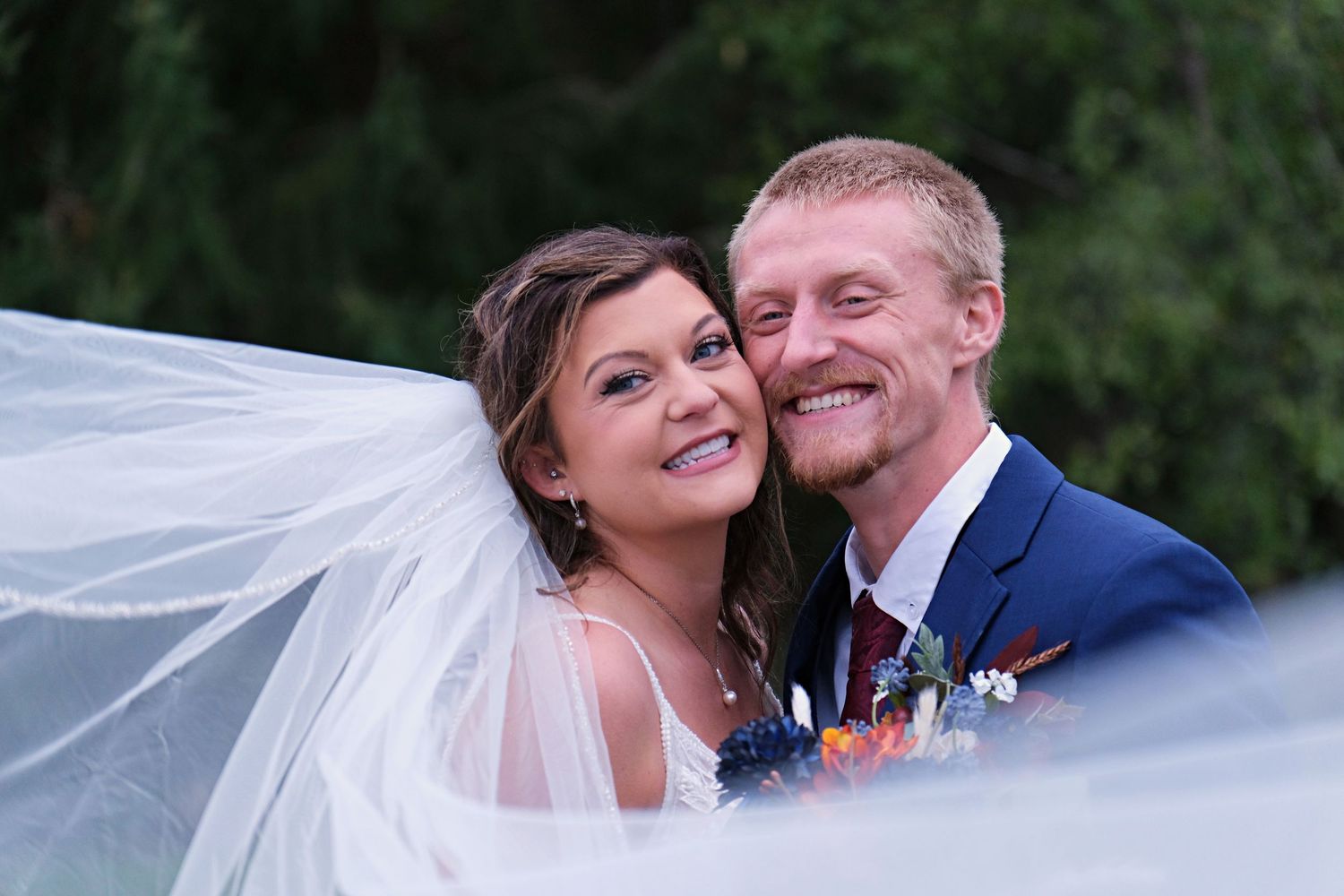 Newlywed couple sharing intimate moments outdoors with flowing veil in sunset light.