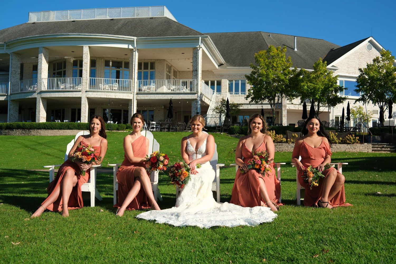 Wedding party poses on green lawn with white colonial style building in background.