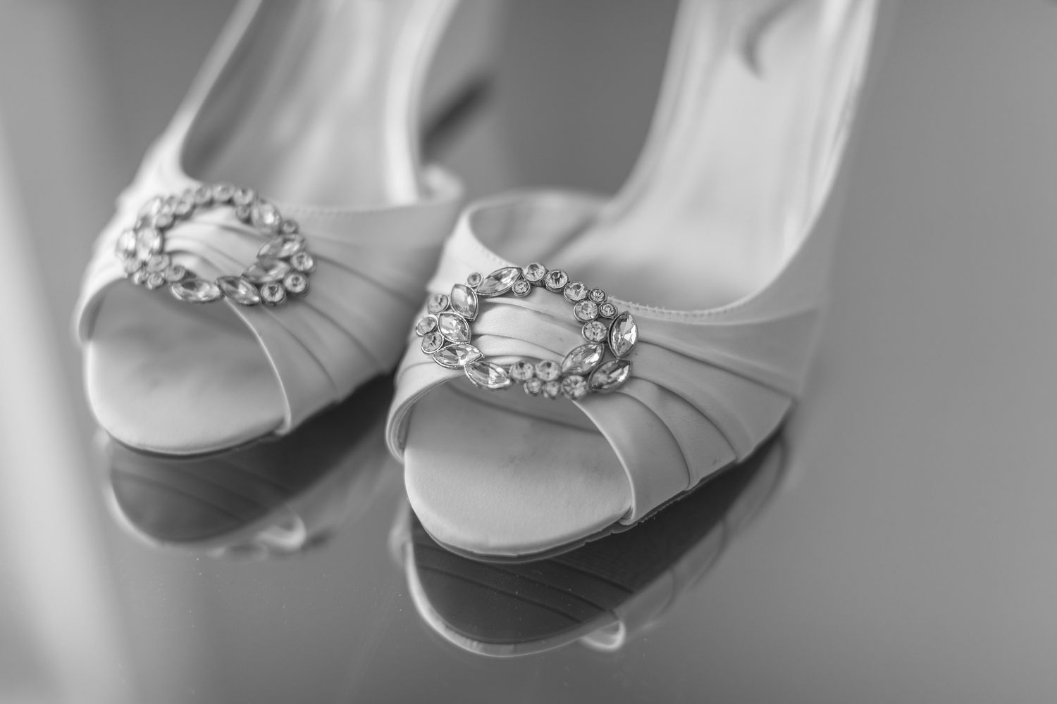 Elegant white bridal shoes with crystal embellishments arranged in a row on a light surface.