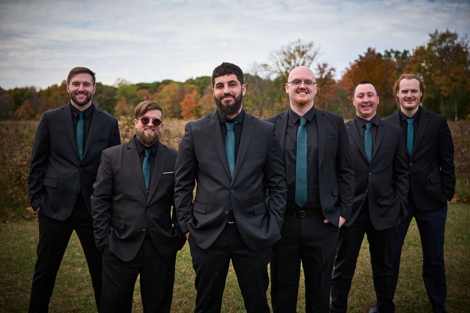 Wedding party in black suits posing together during an autumn outdoor photoshoot.