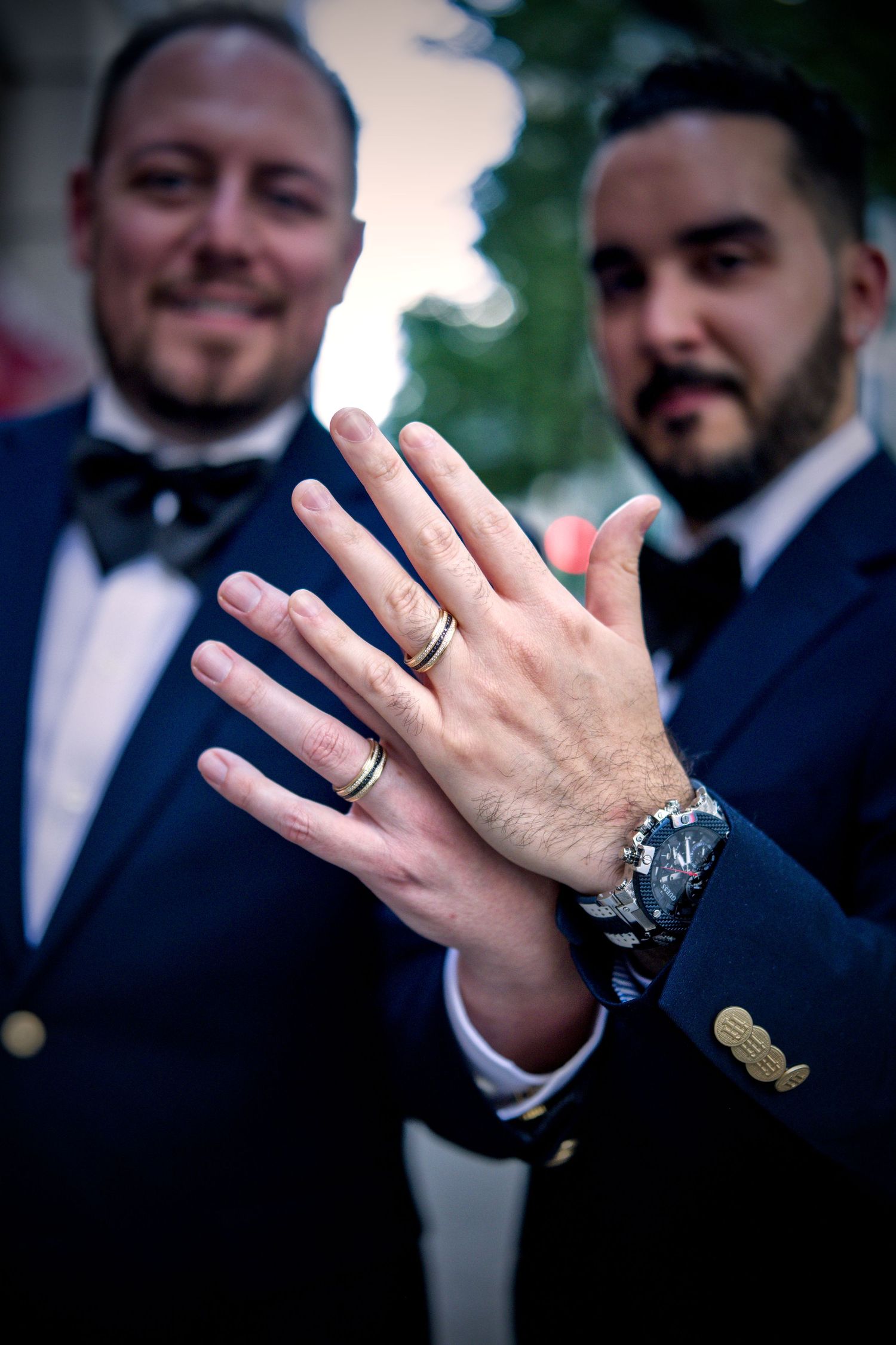 Close-up shots of hands displaying wedding rings against dark formal attire.