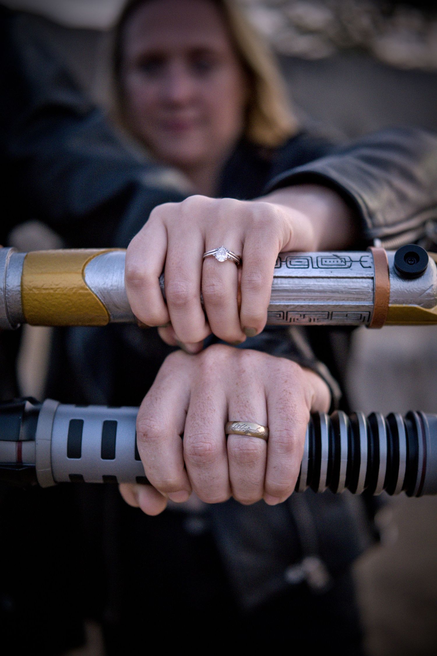 Close-up of hands wearing wedding rings while holding a lightsaber prop.