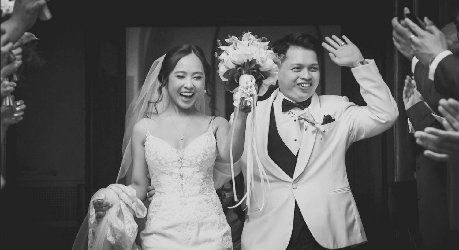 A black and white wedding celebration scene with guests clapping and cheering.