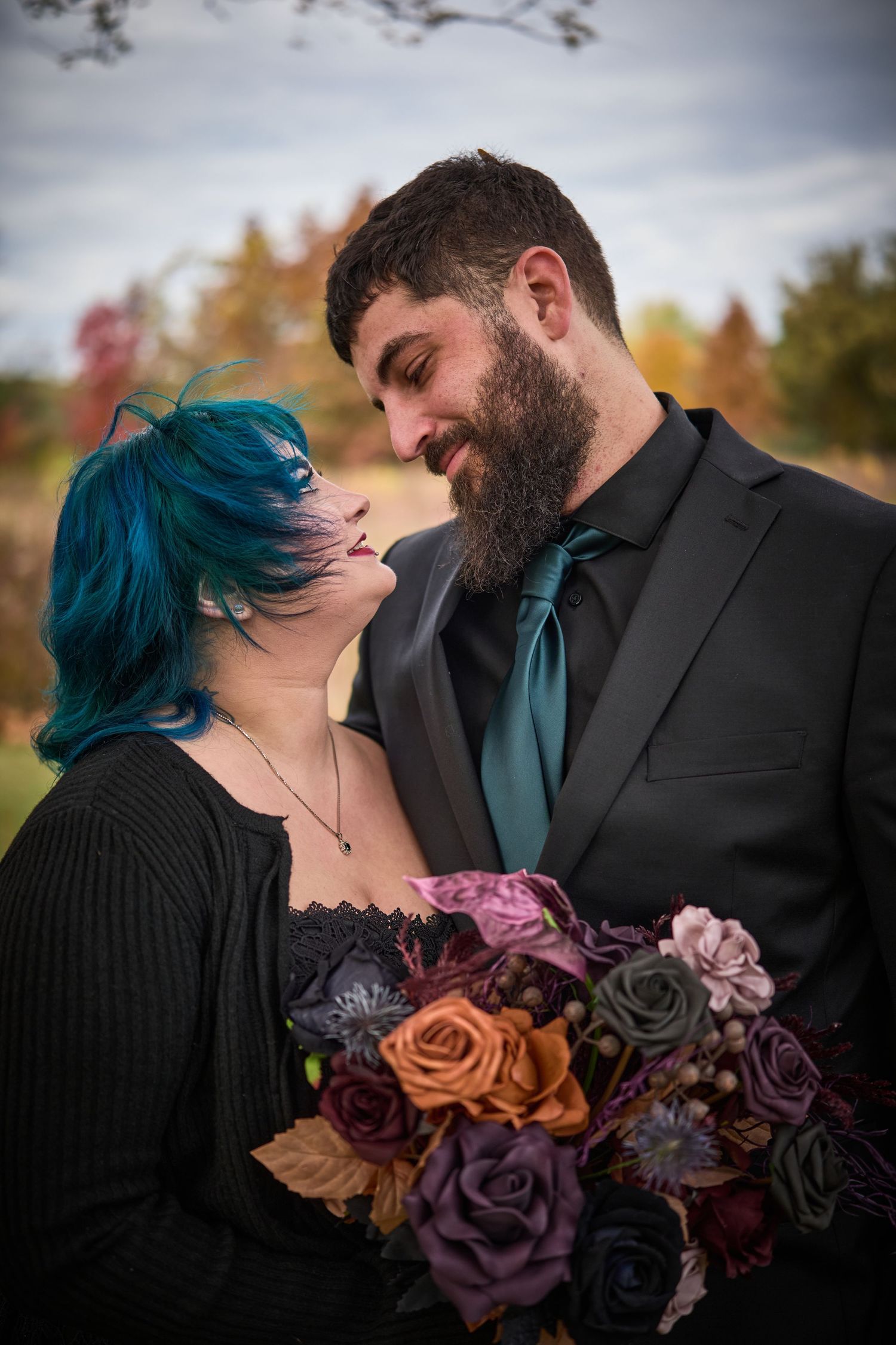Close-up of a couple with colorful autumn roses and unique blue hair sharing an intimate moment.