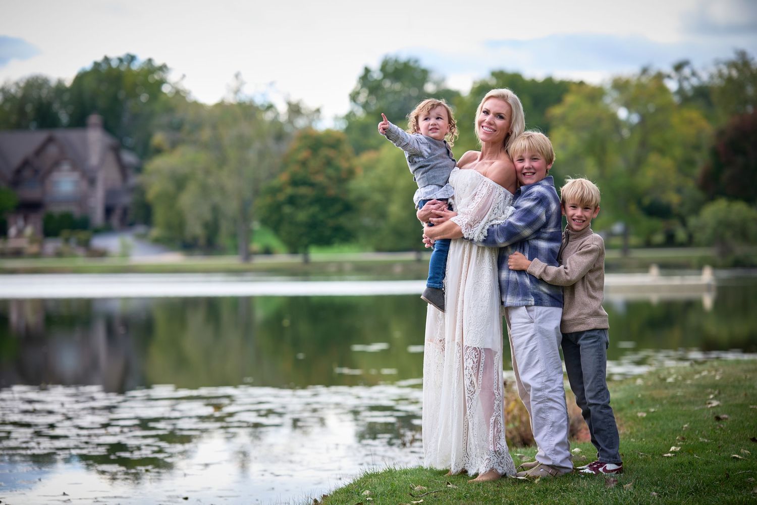 Family portrait of a woman with three children standing by a serene lake surrounded by lush green trees.