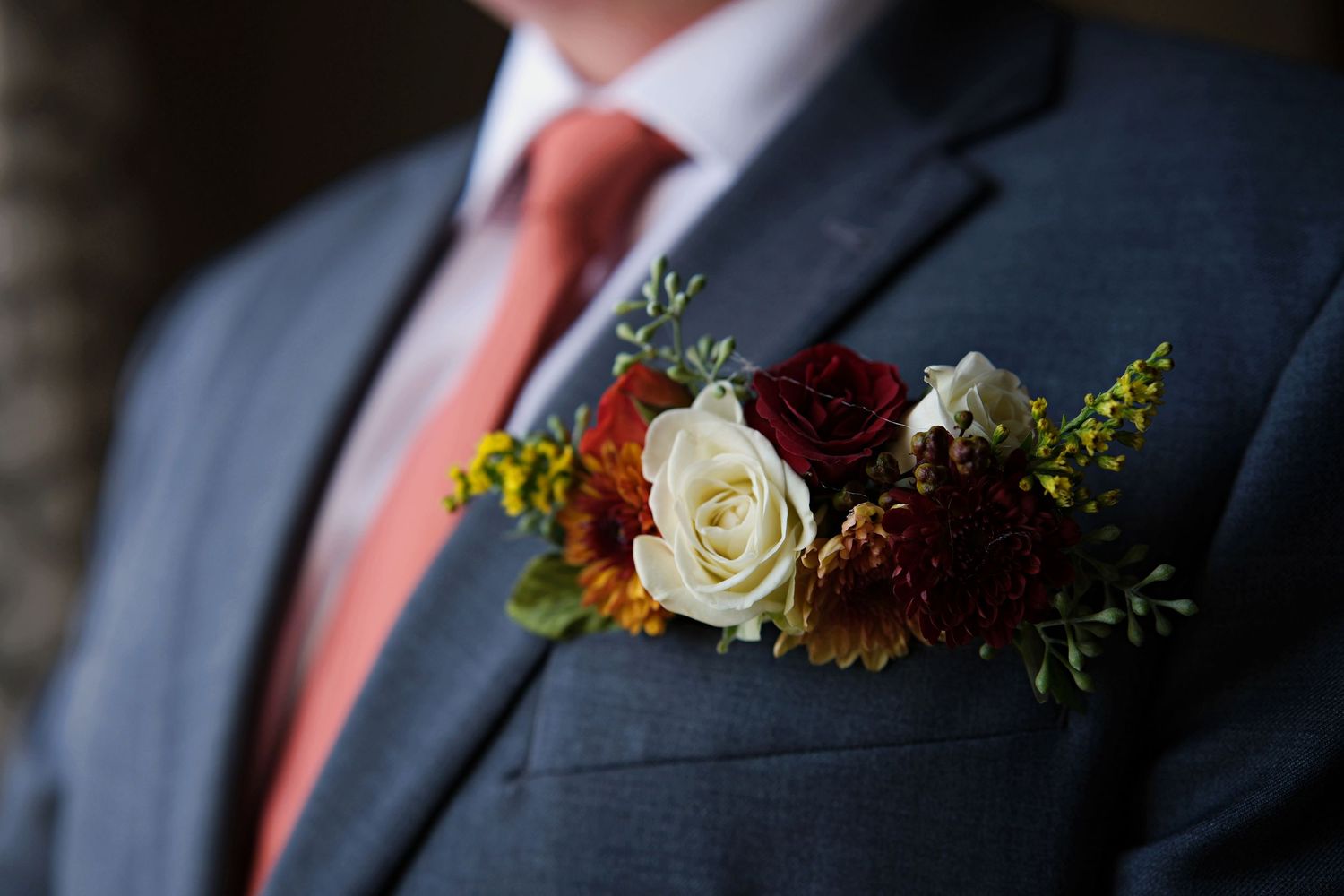 Close-up details of coral boutonnieres on charcoal gray suit jackets.