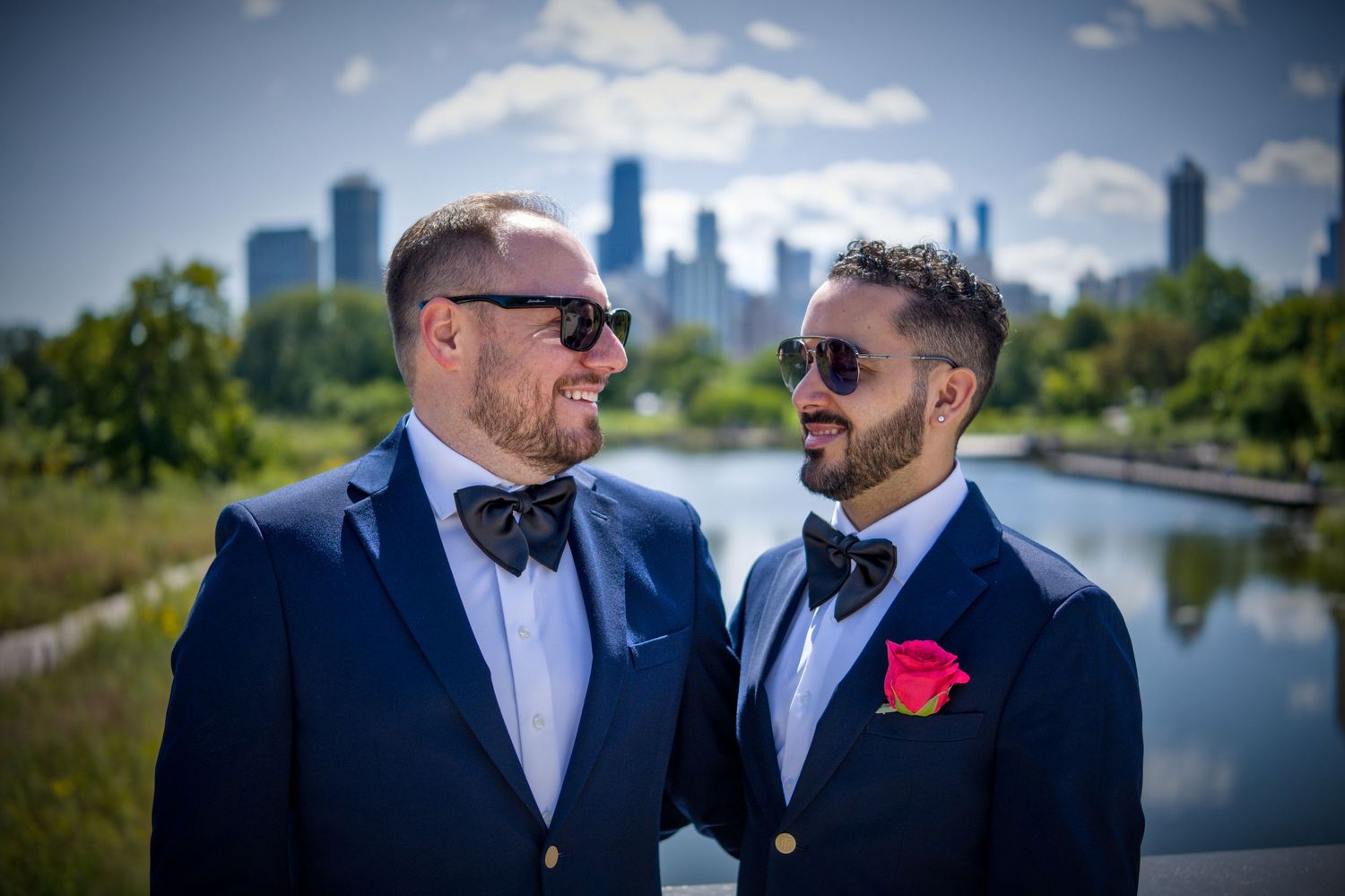Couples in navy suits pose together with city waterfront in the background.