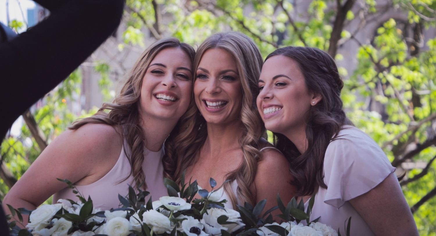 Joyful bridesmaids sharing laughs outdoors during wedding celebration.