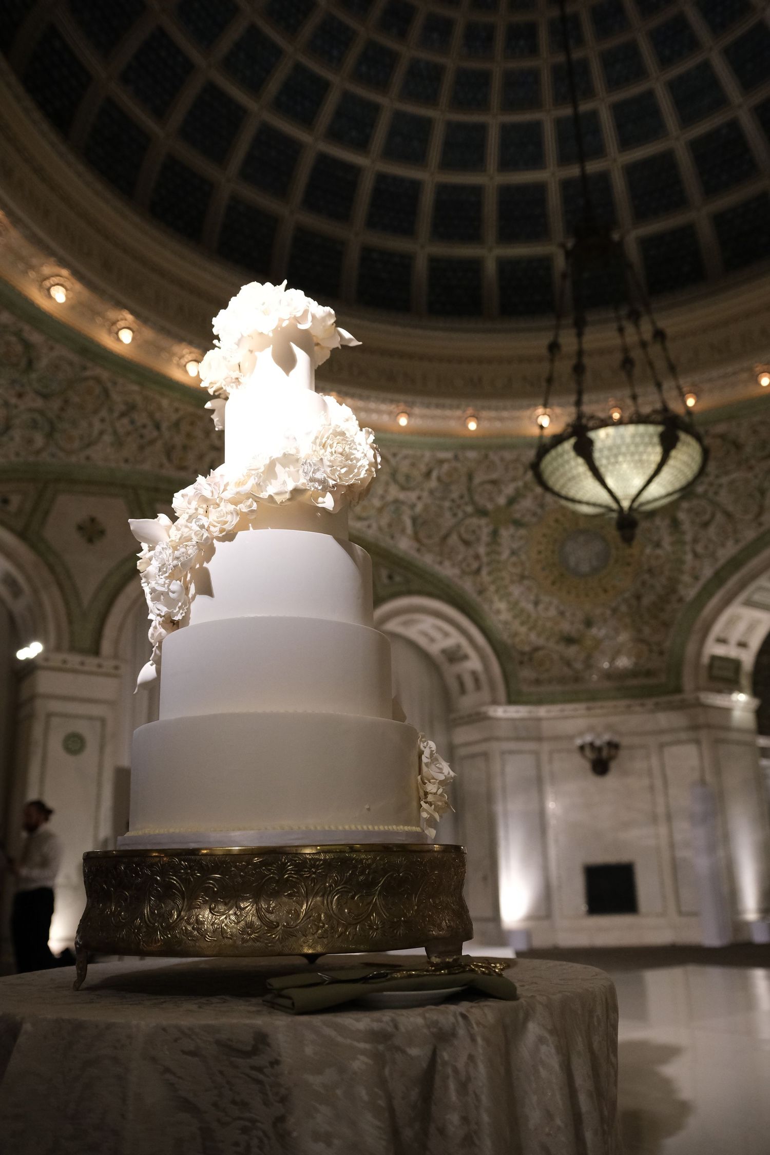 An elegant white wedding cake displayed under an ornate domed ceiling with classical architecture.