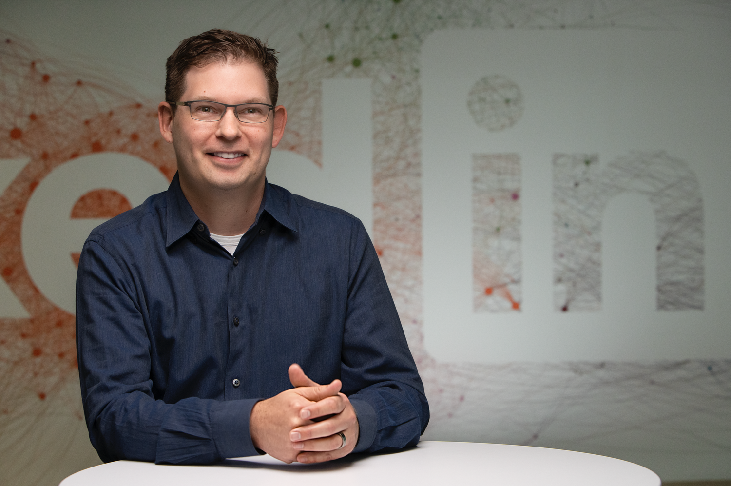 Business professional sitting at a desk with a modern office wall logo backdrop.