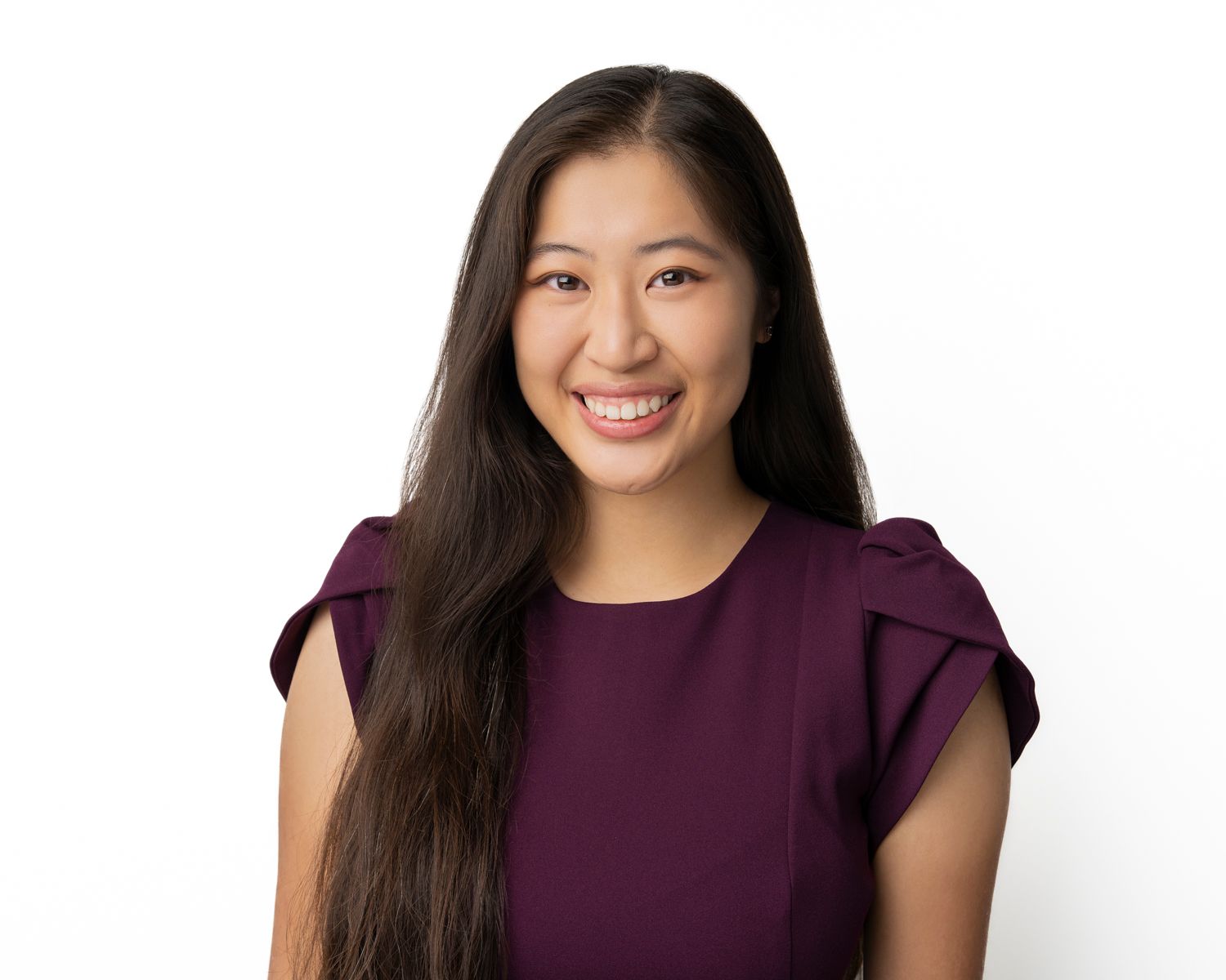 Cheerful professional headshot of a woman wearing a purple top against white backdrop.