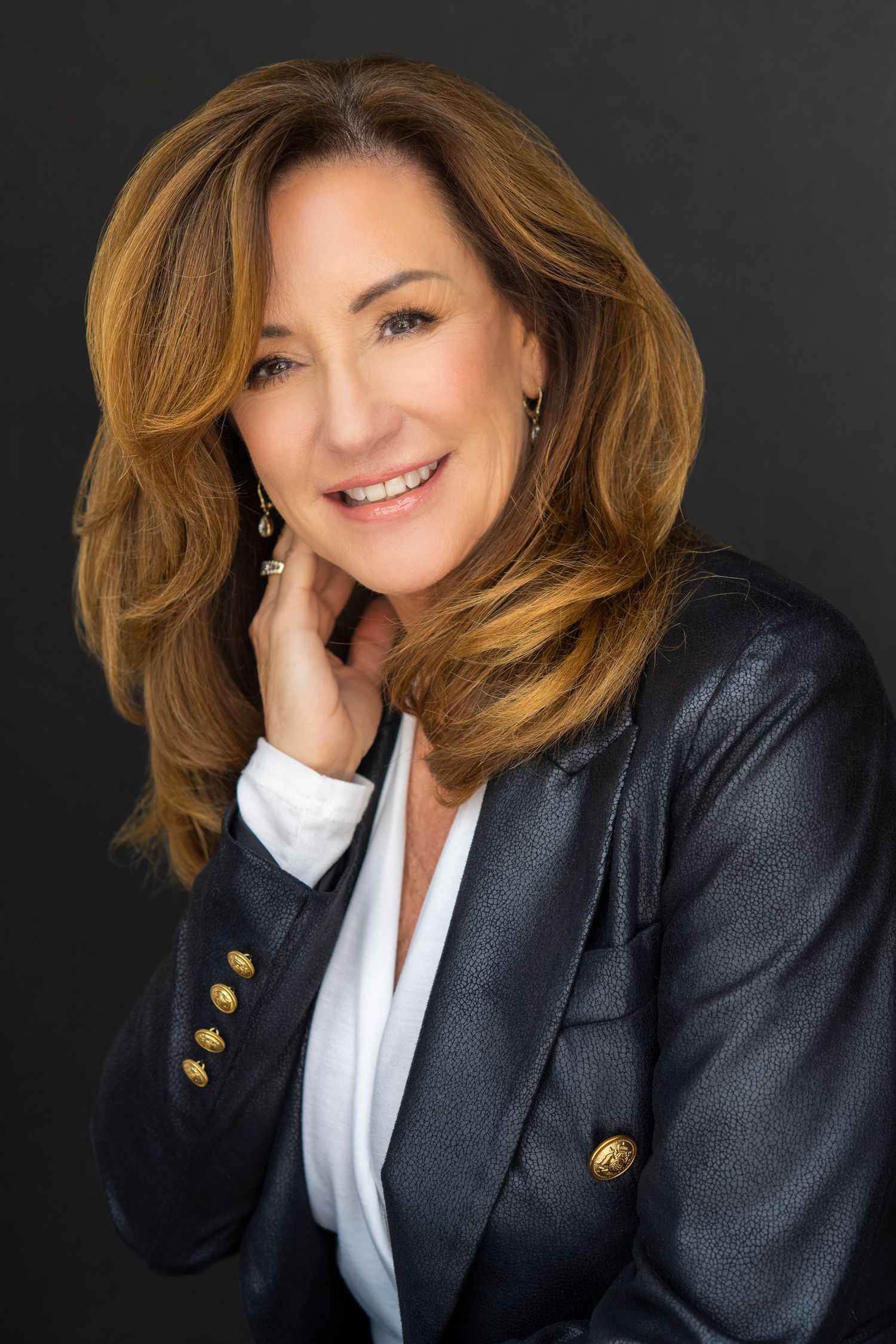 Executive portrait of a woman in black leather blazer with gold buttons against dark background.