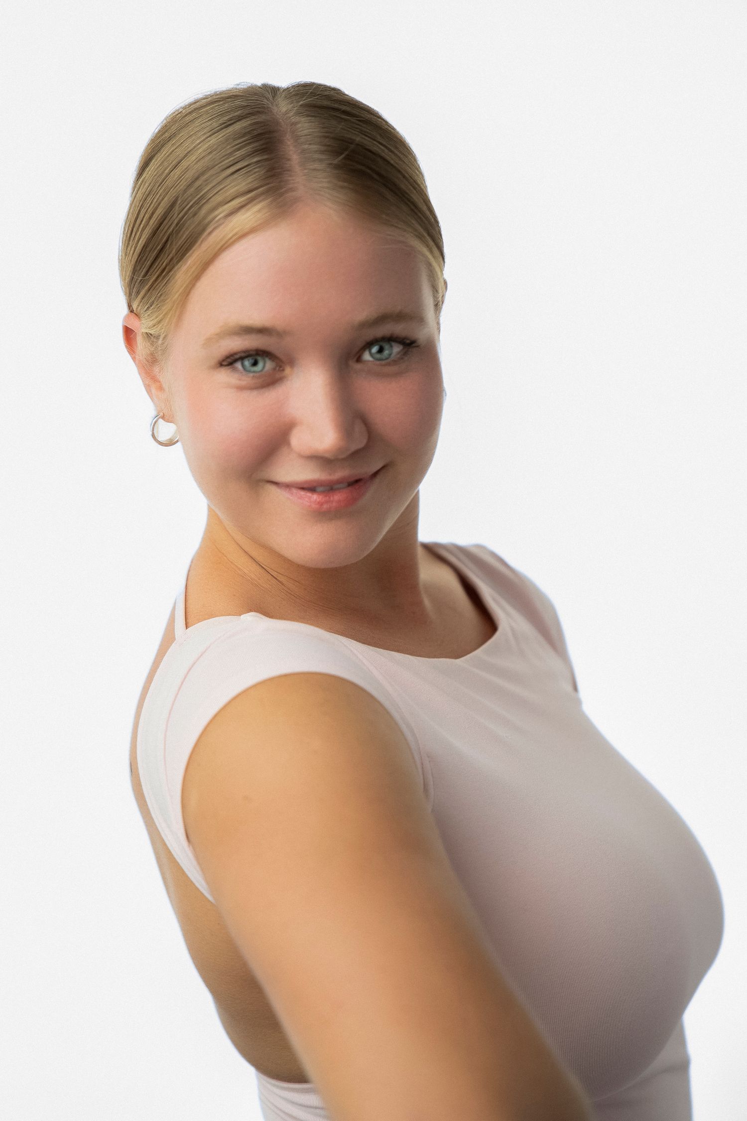 A portrait of someone wearing a white sleeveless top against a light background, smiling warmly at the camera.