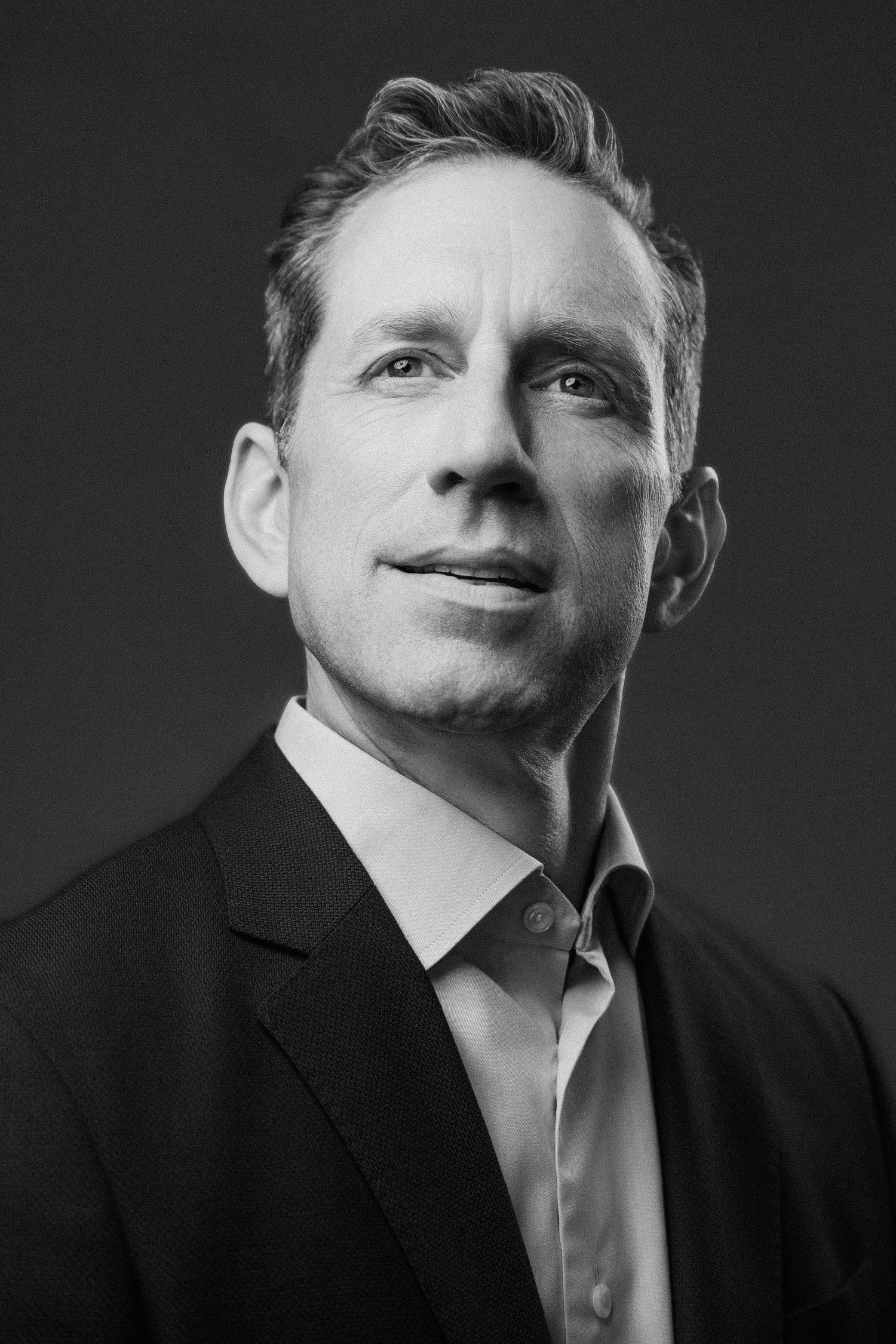 Black and white professional portrait of a middle-aged man in a blazer, gazing upward confidently.