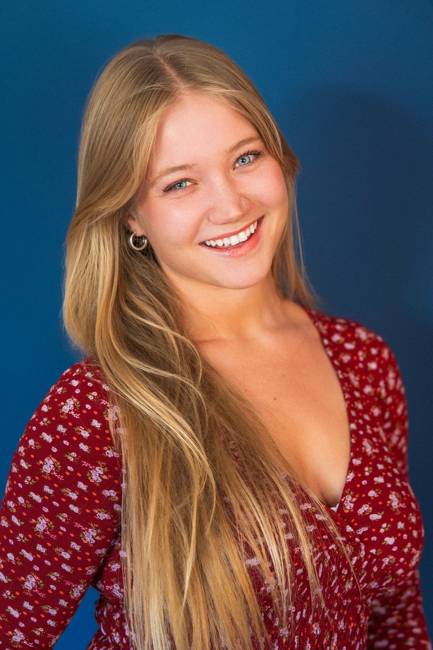 Portrait series showing joyful expressions against blue background wearing red polka dot top with flowing blonde hair.