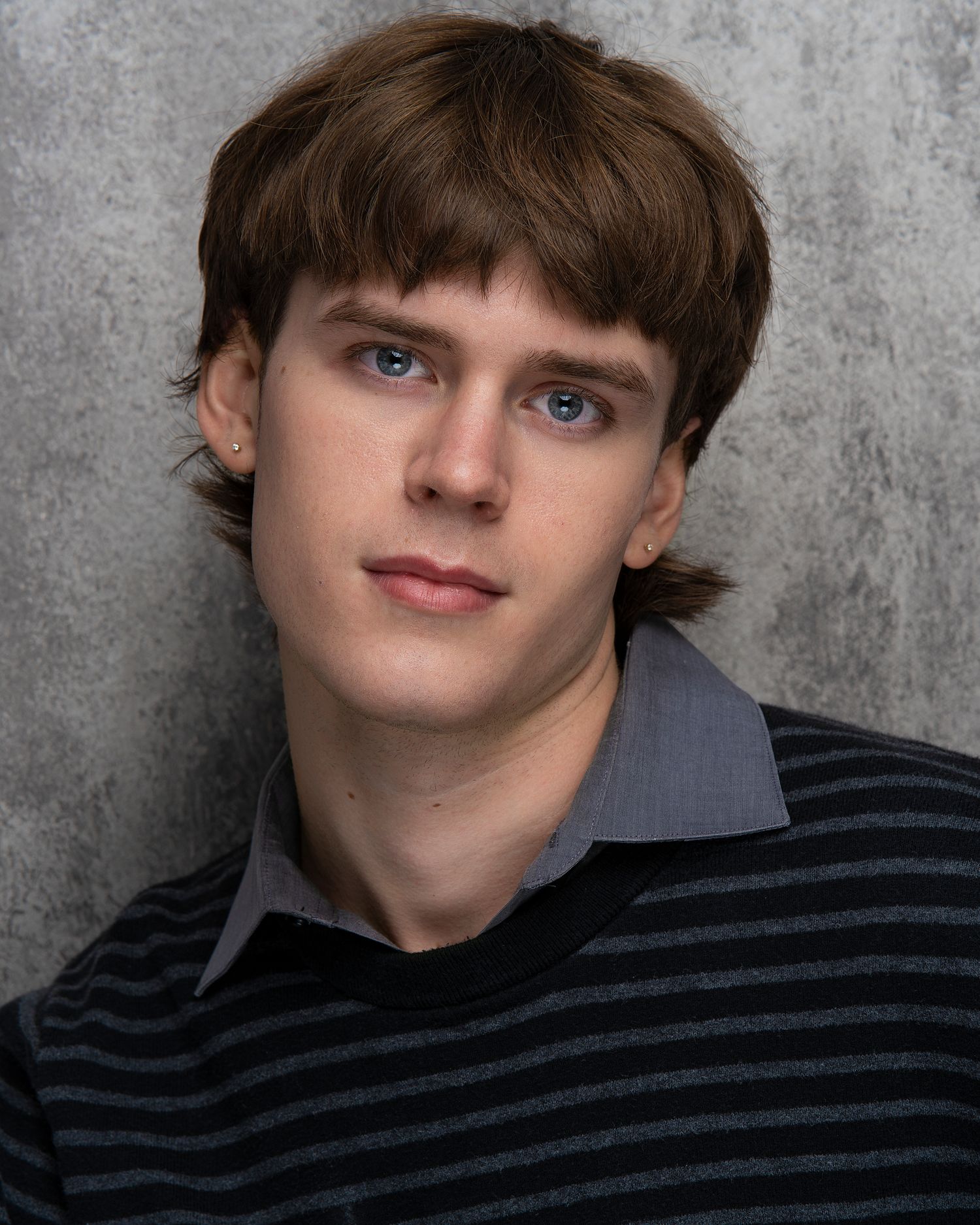 Professional headshot portrait against a gray background featuring a young person in a striped sweater.