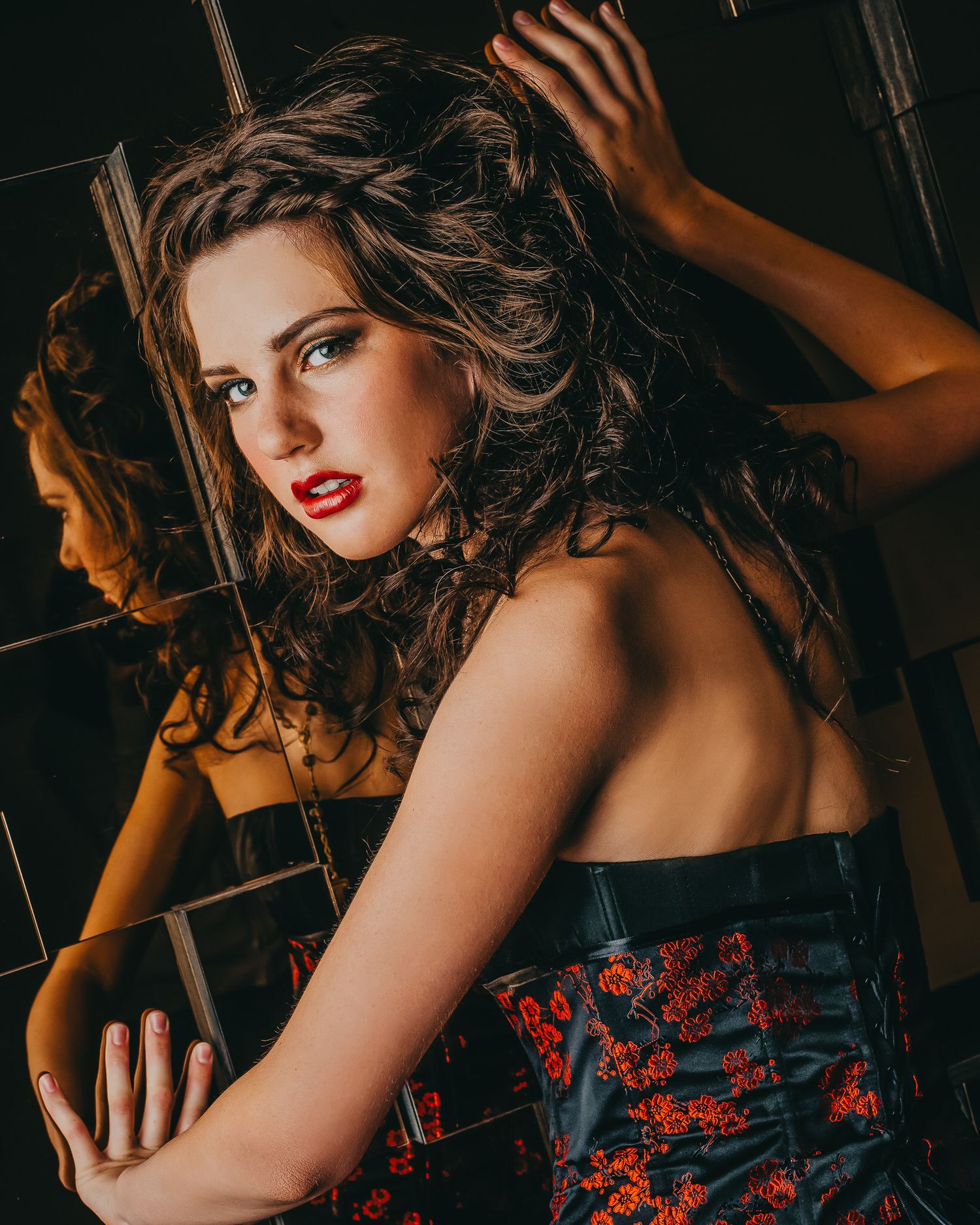 A moody fashion portrait in dark lighting shows a woman in a red and black floral dress with dramatic styling.