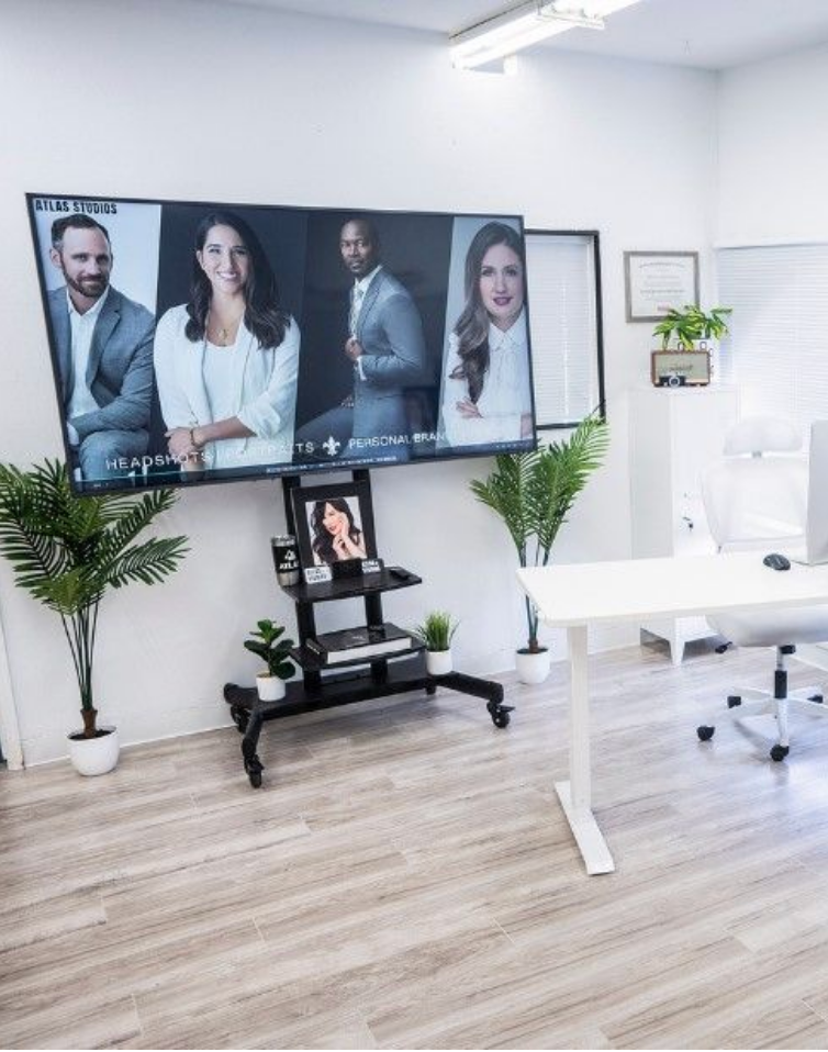 Modern office space with large display screen and plants on hardwood floor.