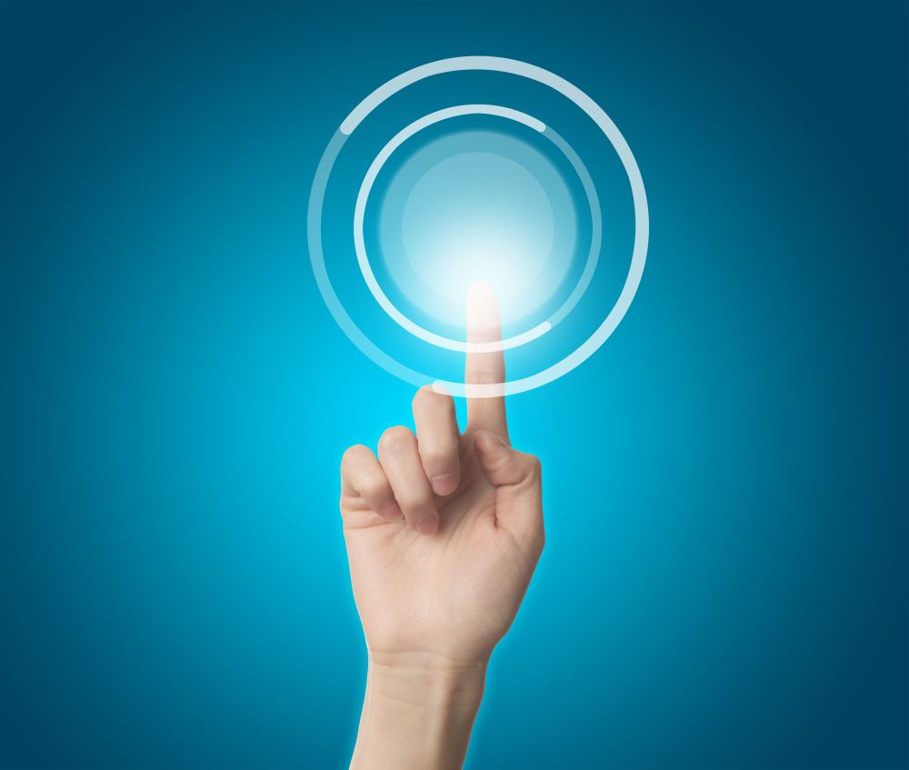 Hand touching glowing blue circular button interface on turquoise background.