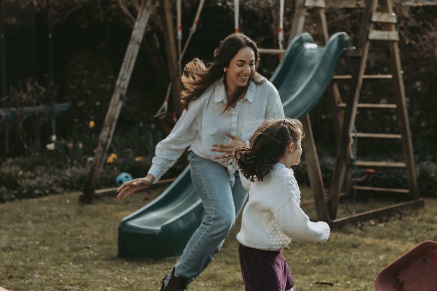 A playful chase around a backyard playground slide on a cloudy day.