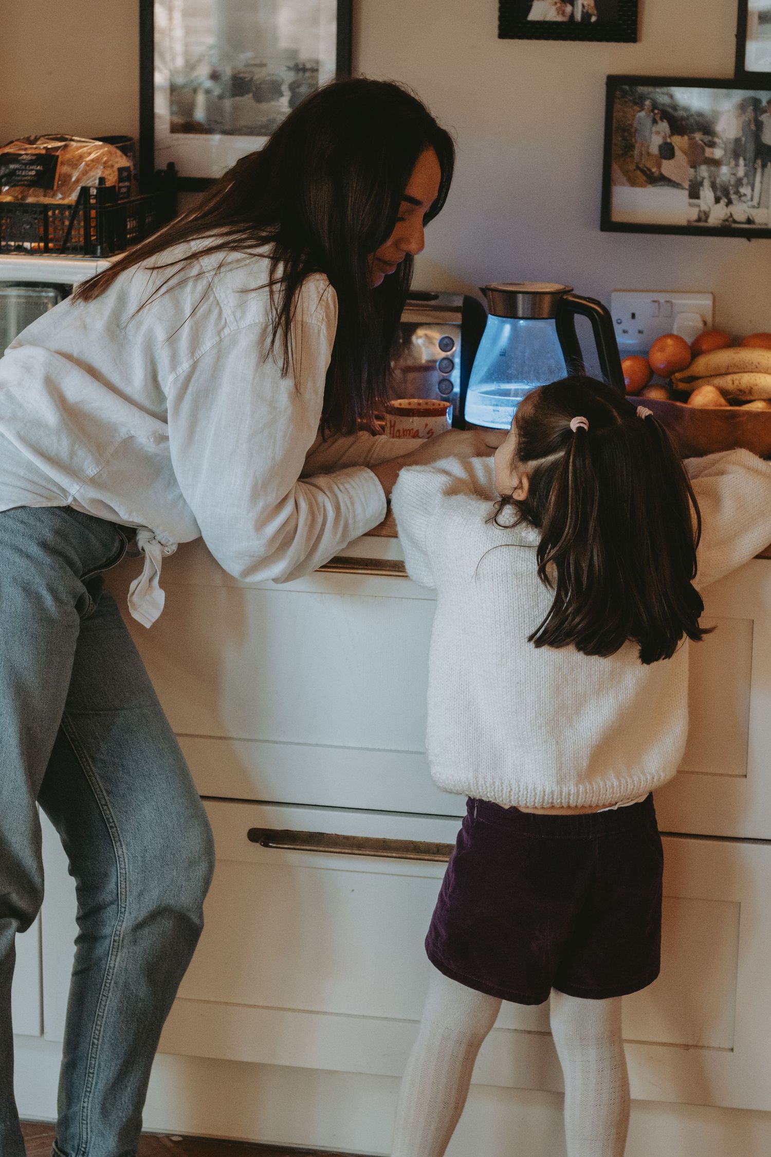 A parent and child share a moment in the kitchen while getting something from the drawer.