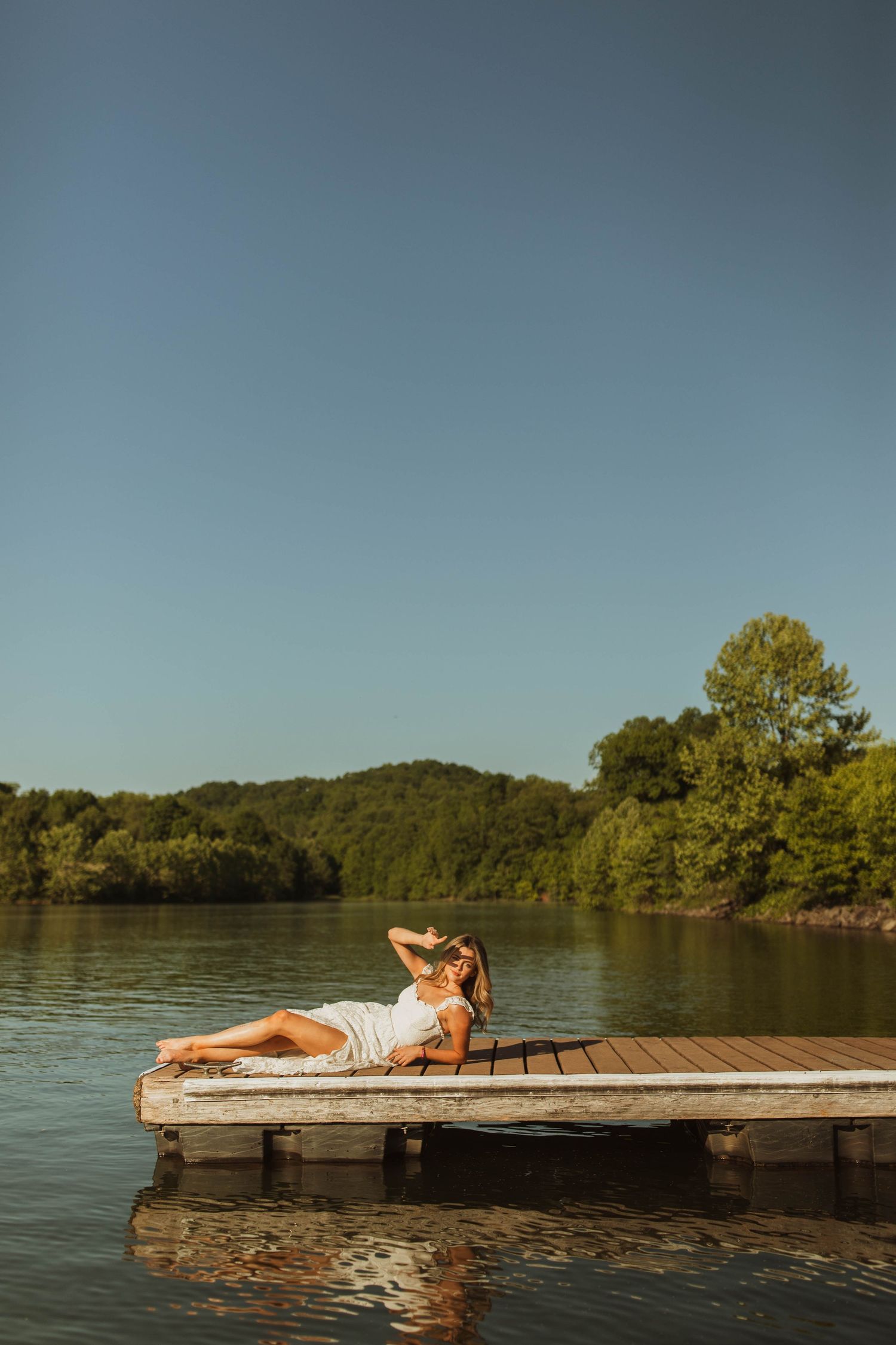 Peaceful summer scene of someone relaxing on a wooden dock over a serene lake.