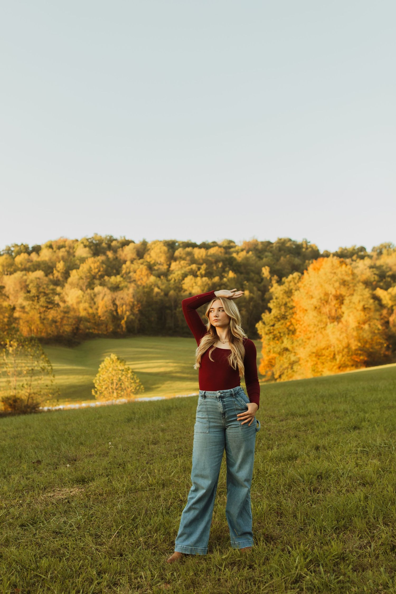 Retro style outfit with wide-leg jeans and burgundy top against golden autumn hillside.