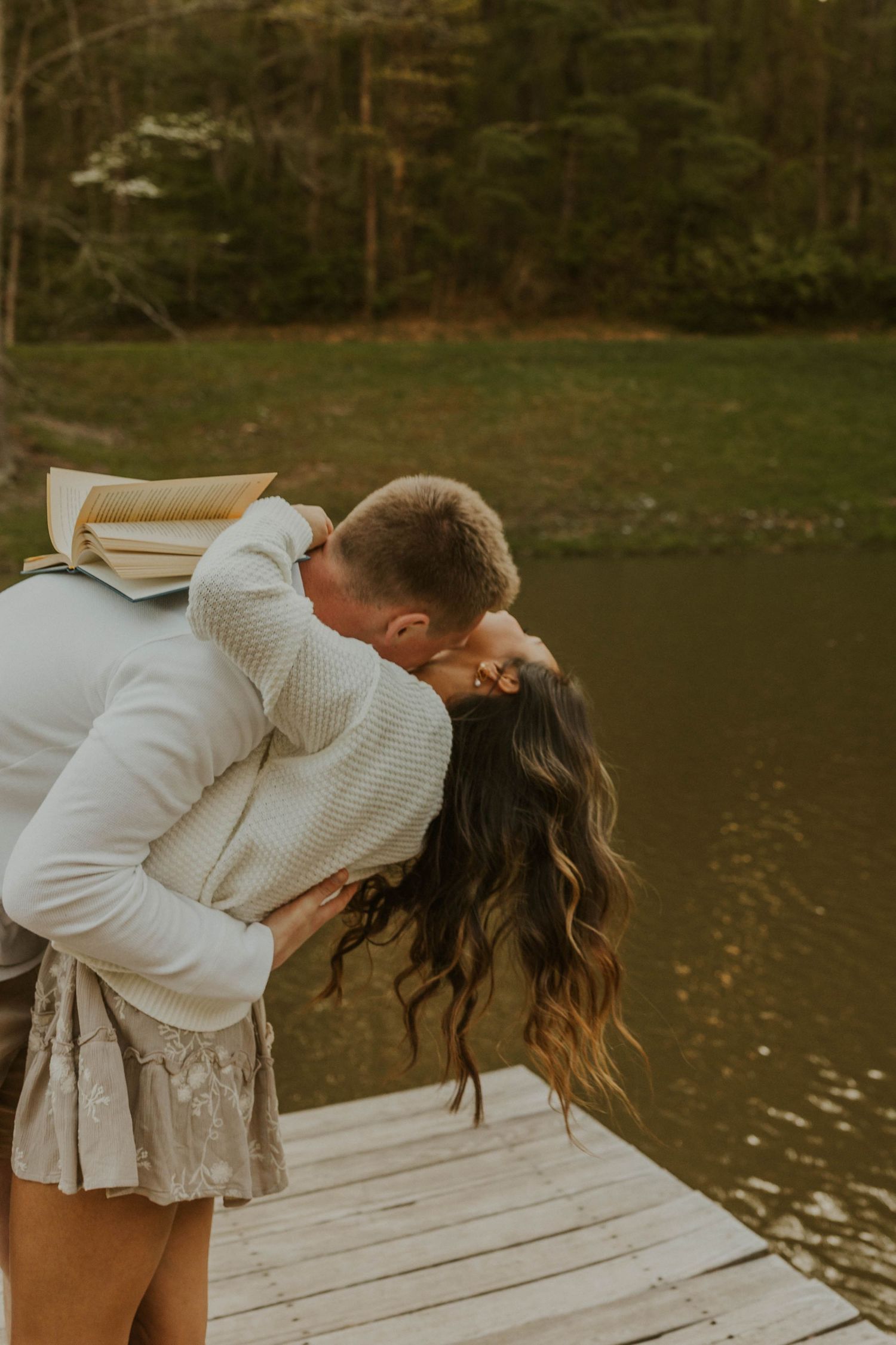 Romantic embrace on wooden dock overlooking serene lake at sunset.