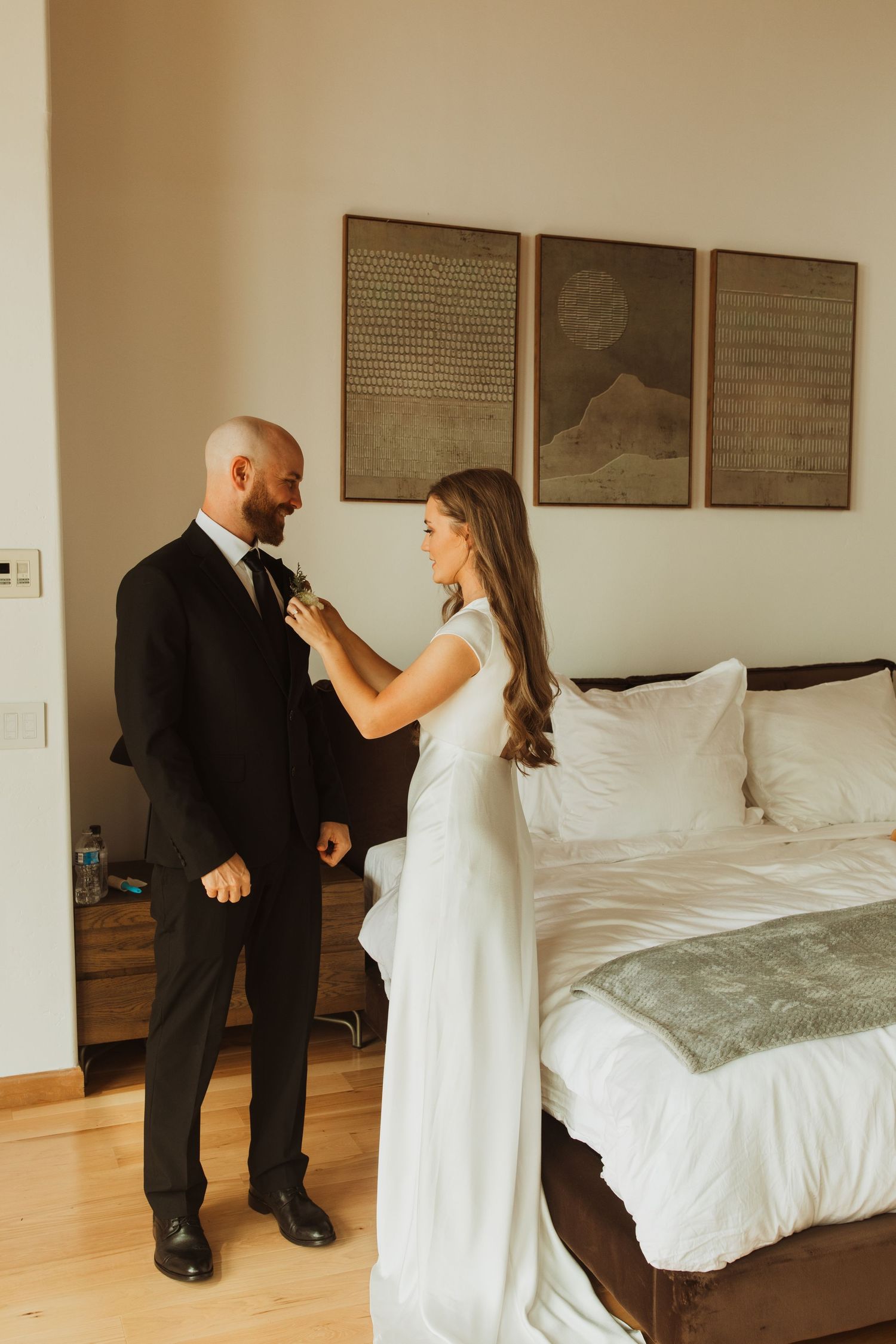 Intimate getting ready moment in a modern bedroom with minimalist wall art.