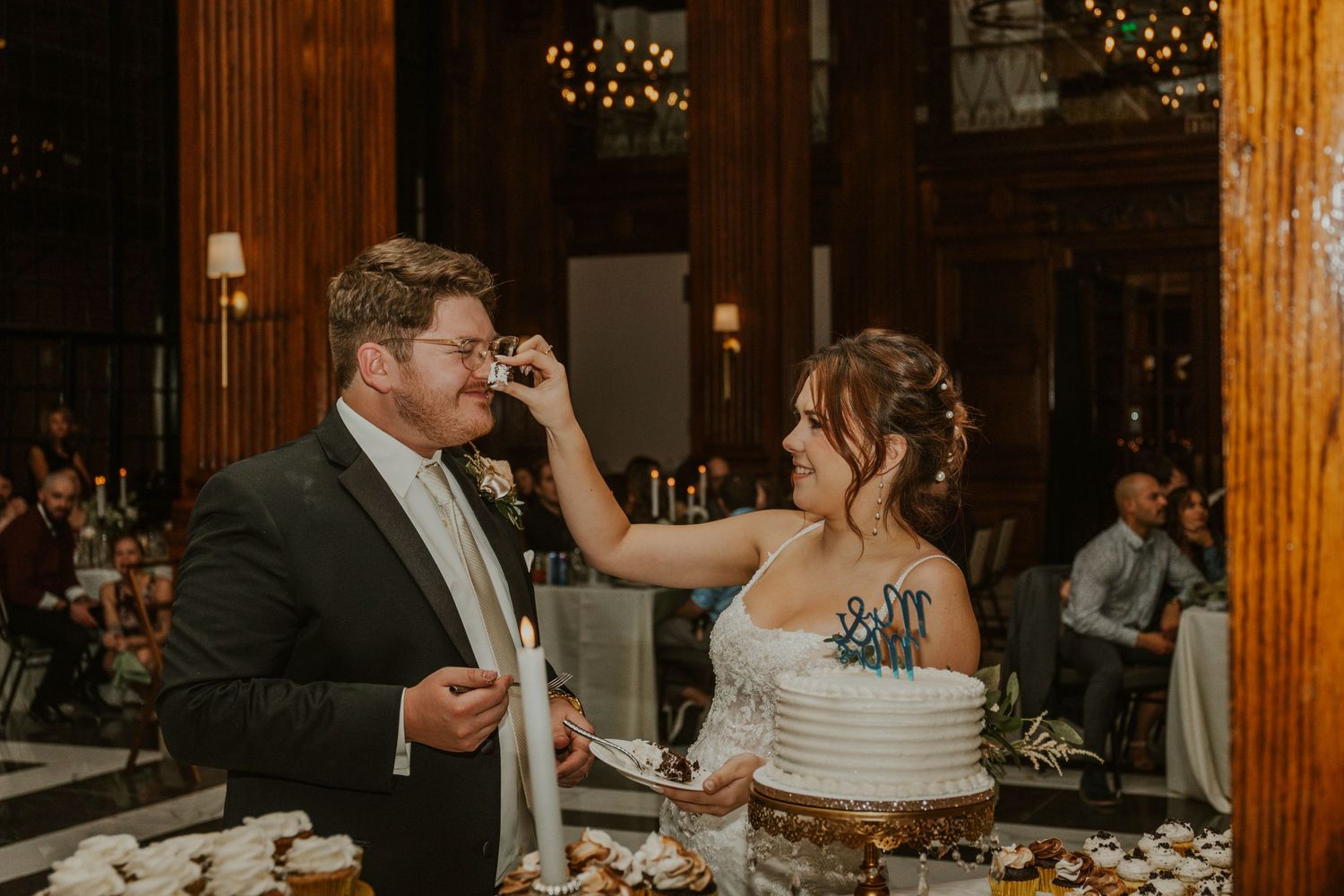 A playful cake-cutting moment at an elegant wedding reception with dark wood decor.