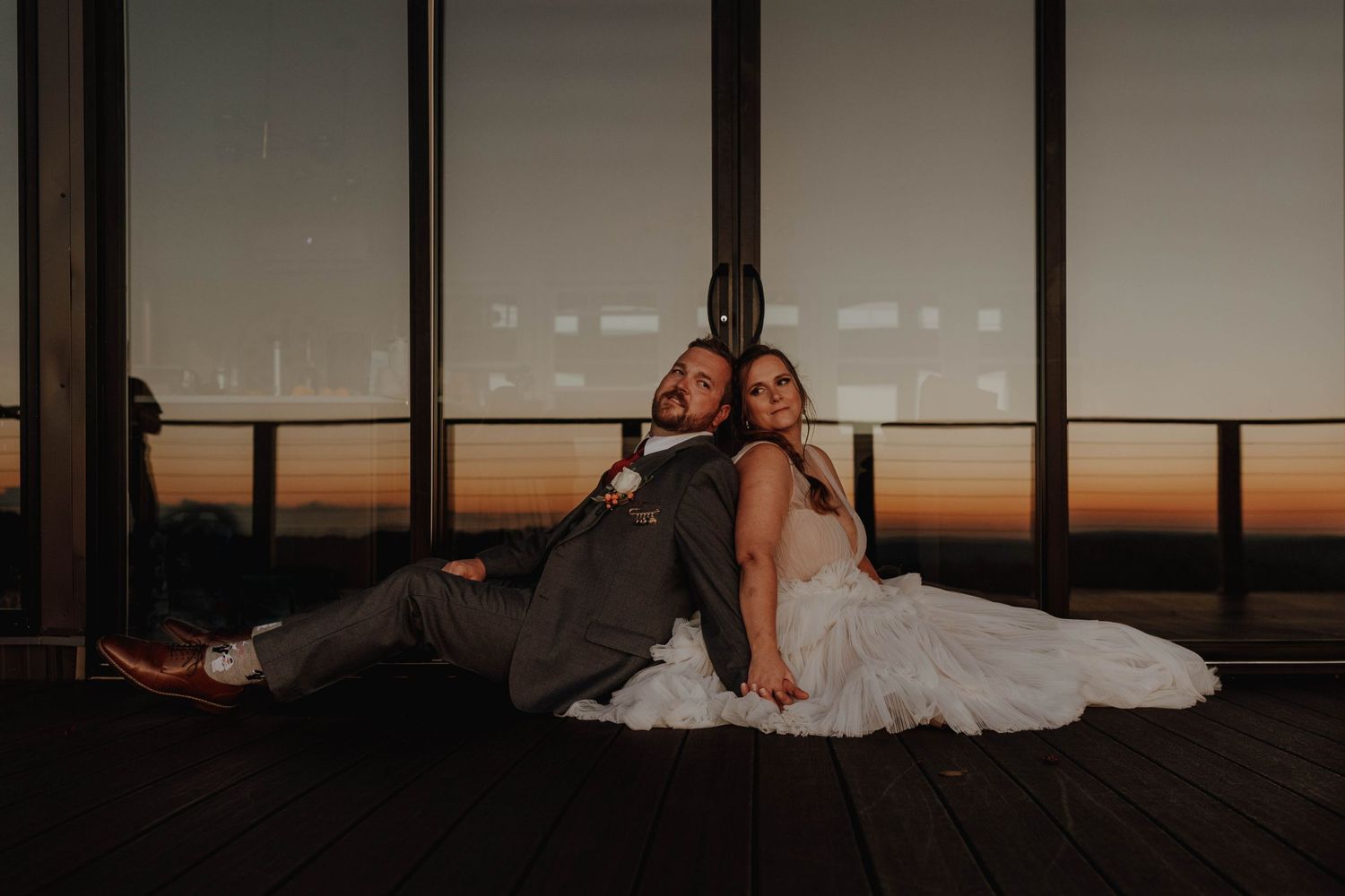 Intimate wedding photo with couple sitting back-to-back against sunset windows.