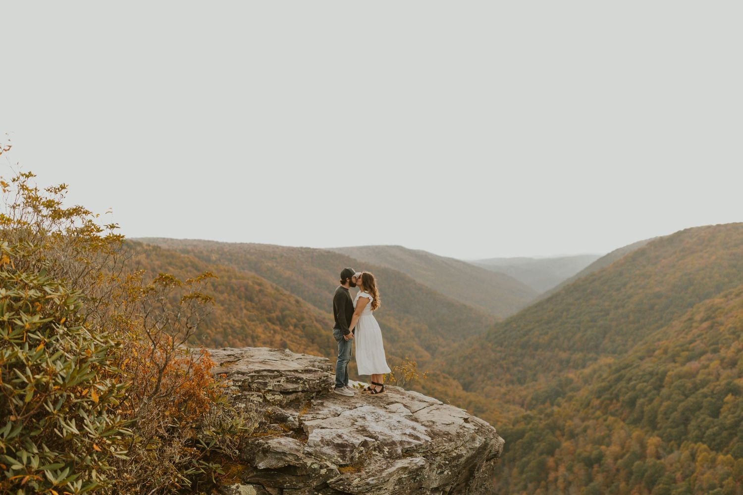 A dramatic mountain vista with a couple standing on a rock outcropping during autumn at lindy point in blackwater falls state park