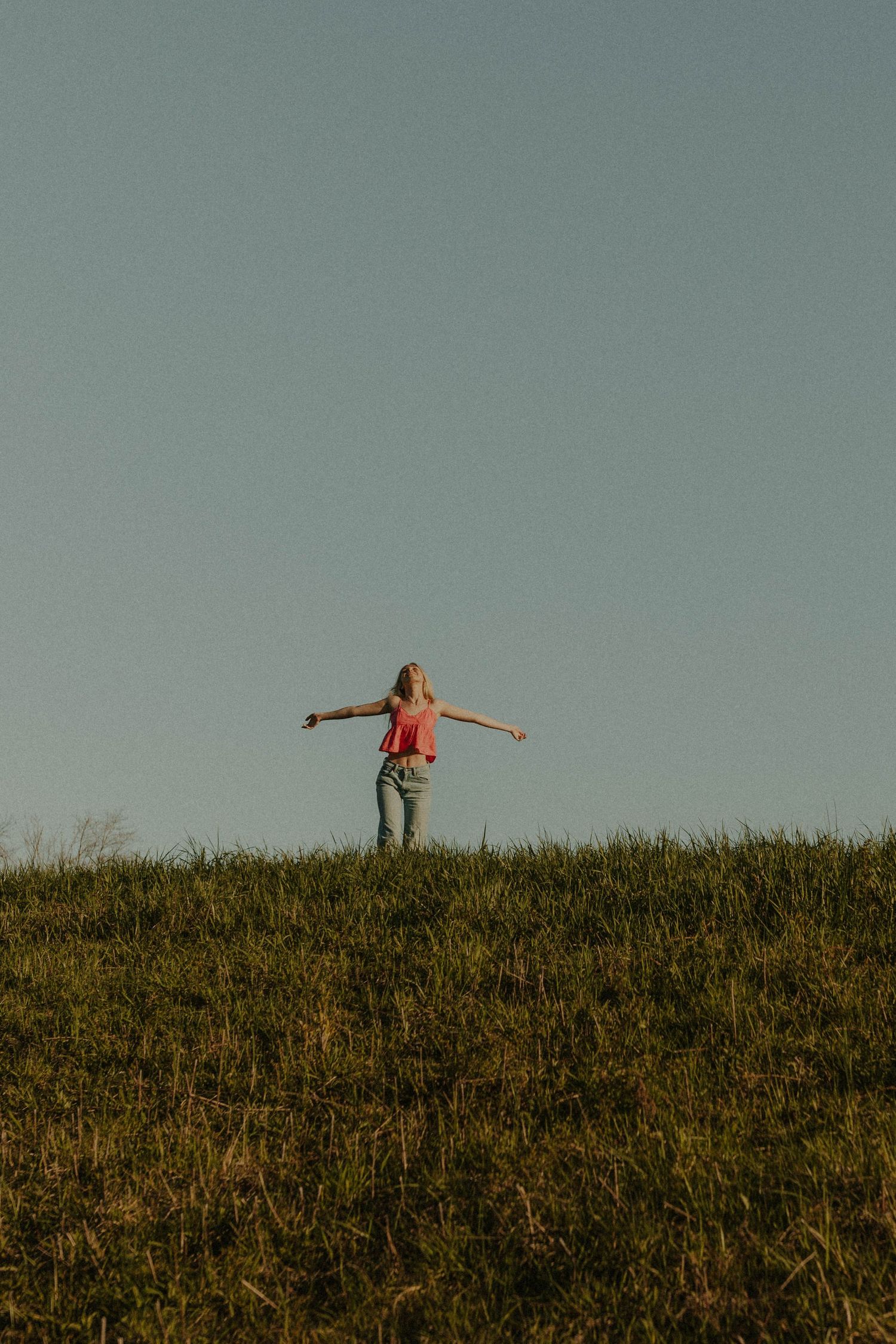 Silhouette against sunset sky with arms outstretched on grassy hilltop.