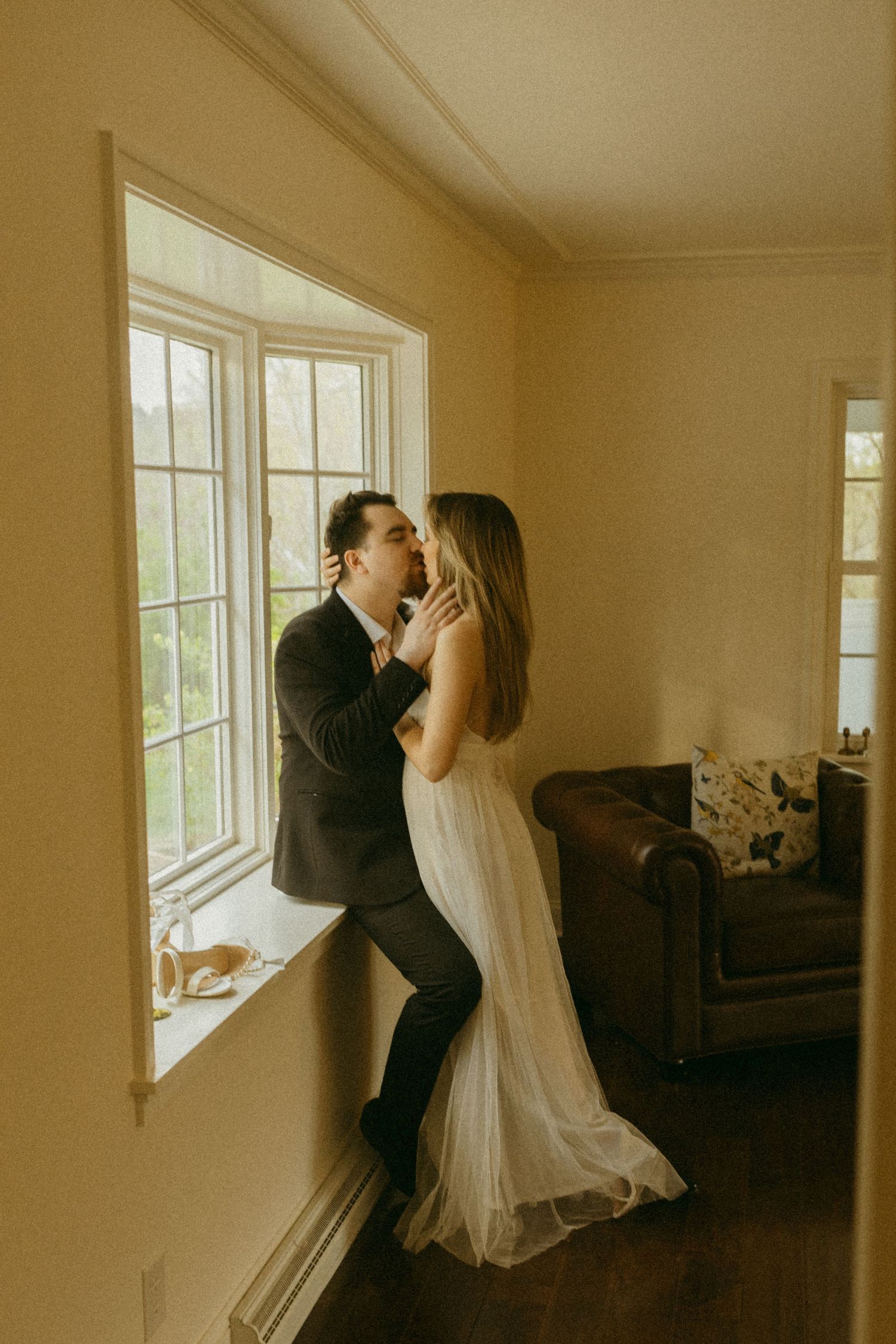 Couple embracing by a window in an intimate indoor setting with vintage decor.