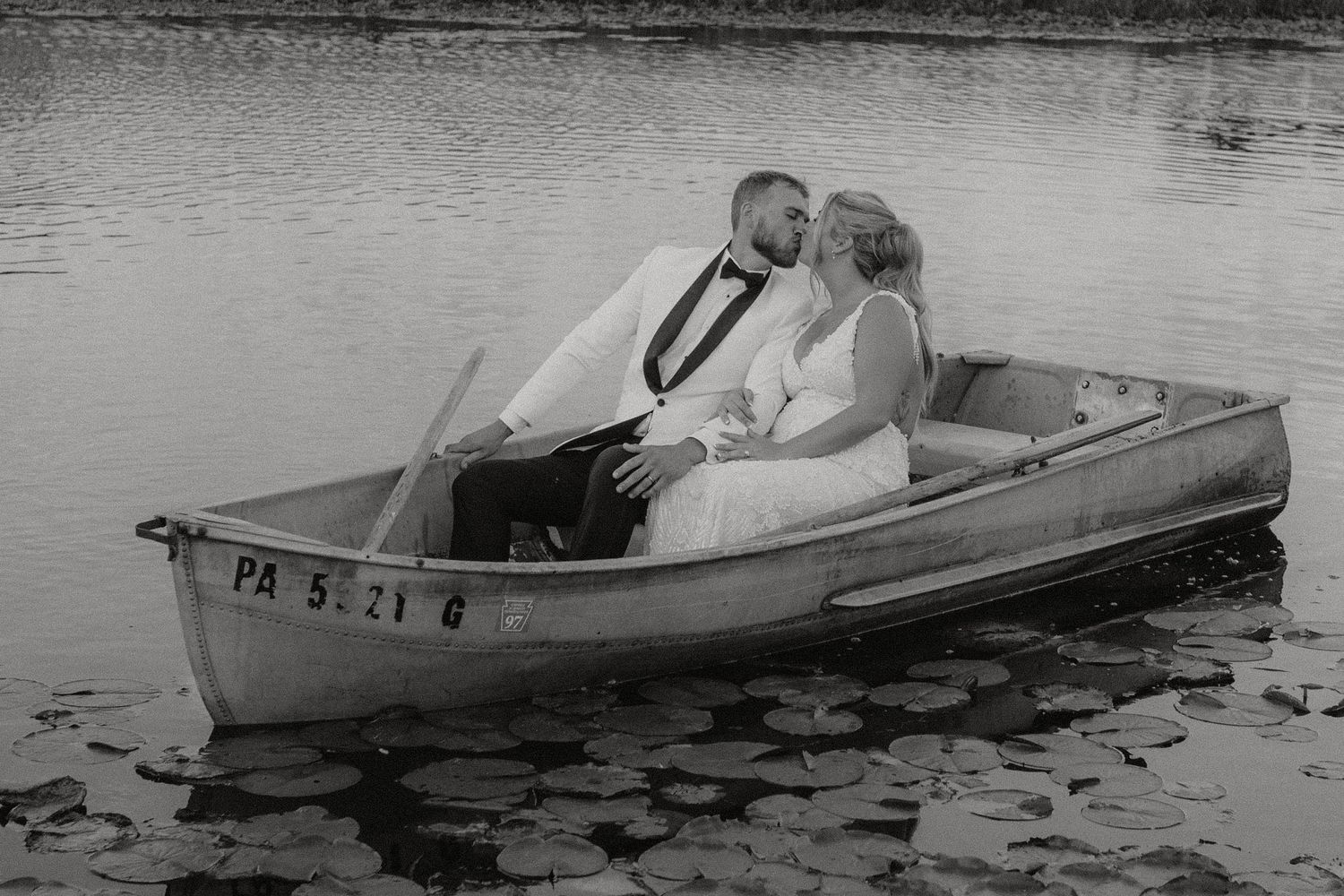 Romantic black and white photo of couple in rowboat on lily-pad covered pond.