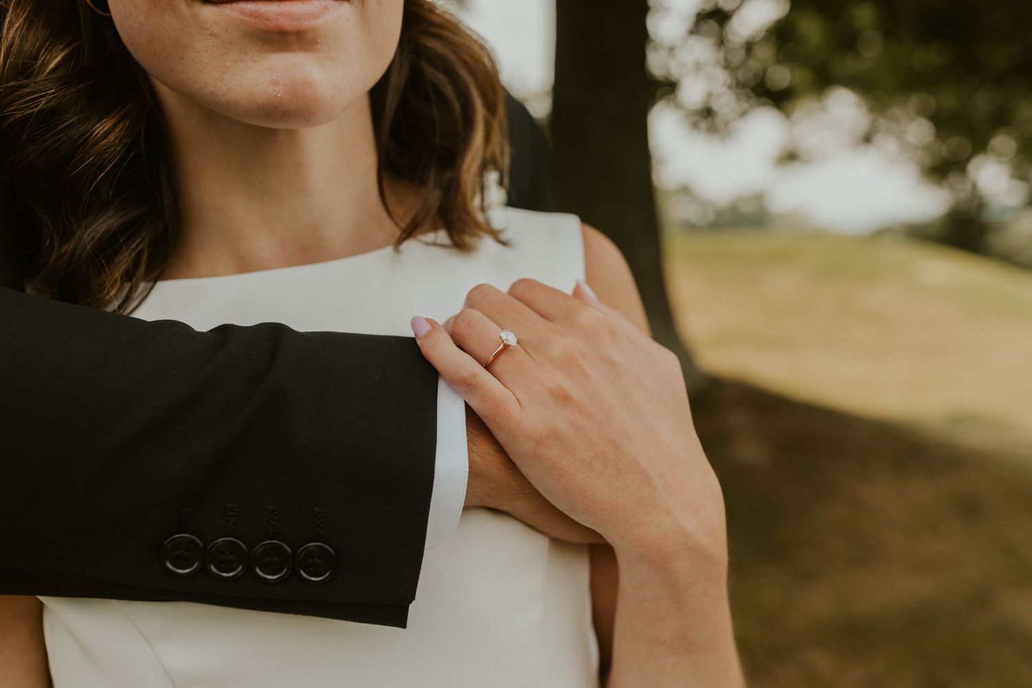 Close up detail of hands and formal attire showing a black suit jacket and white dress.