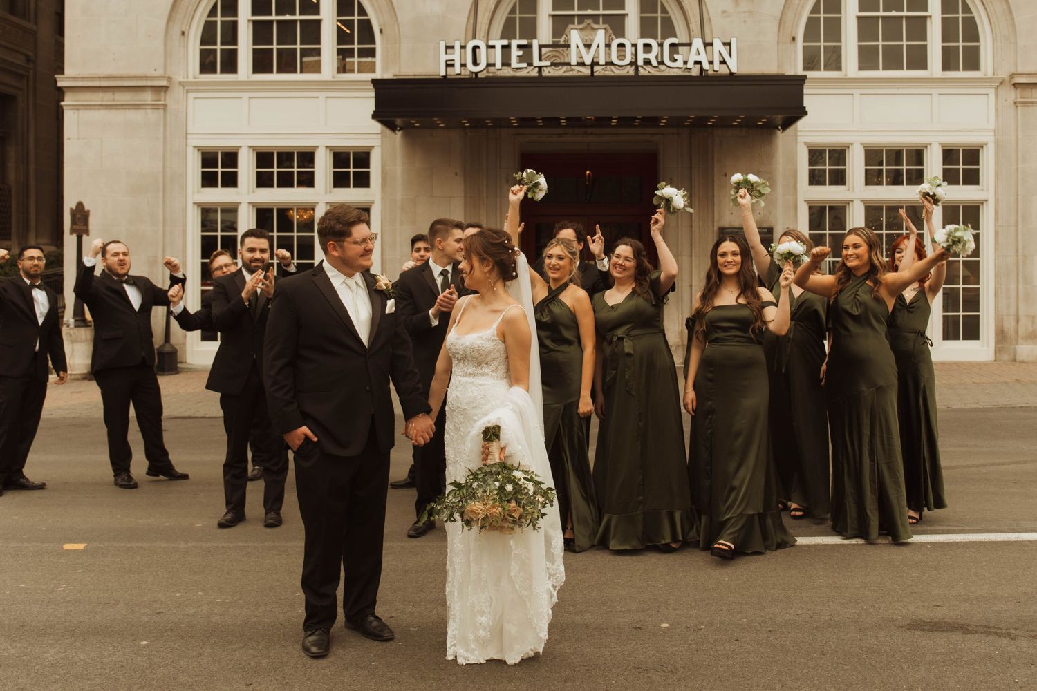 A wedding party celebrates outside Hotel Morgan with bridesmaids in dark dresses raising their arms in joy.