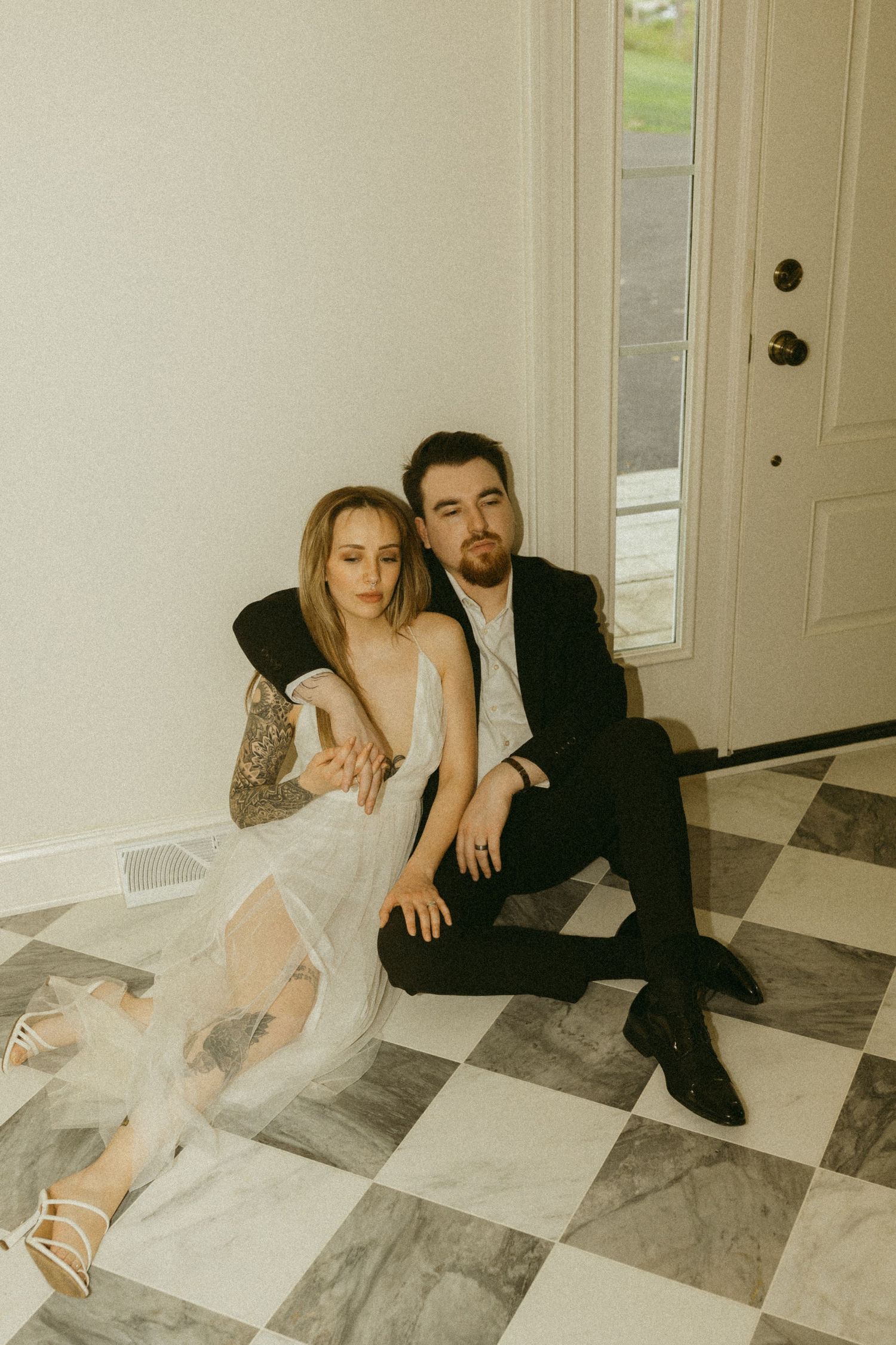 Artistic wedding photo with couple lounging against white wall near doorway.