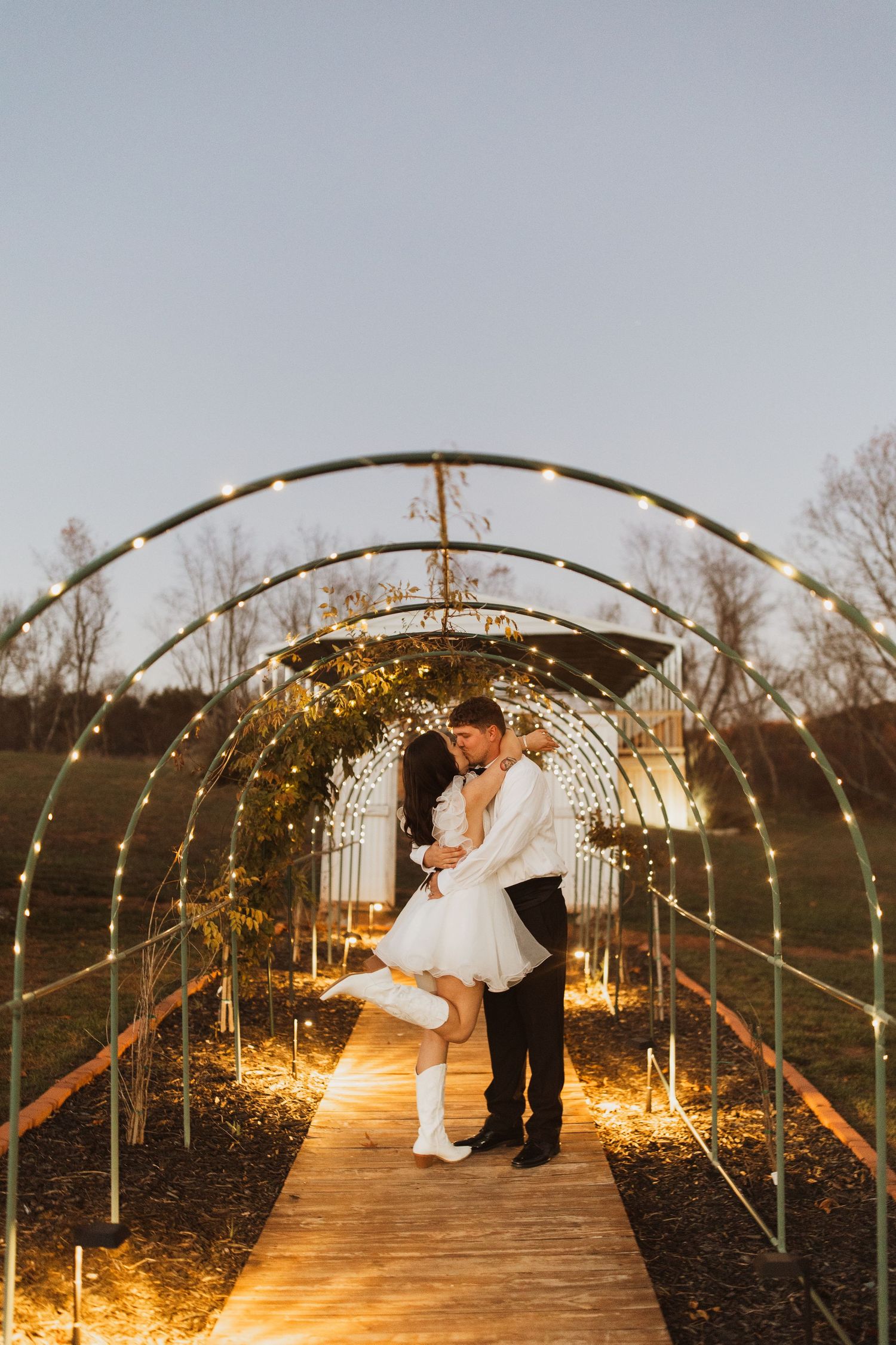 Magical lit archway creates romantic ambiance for wedding portrait at dusk.